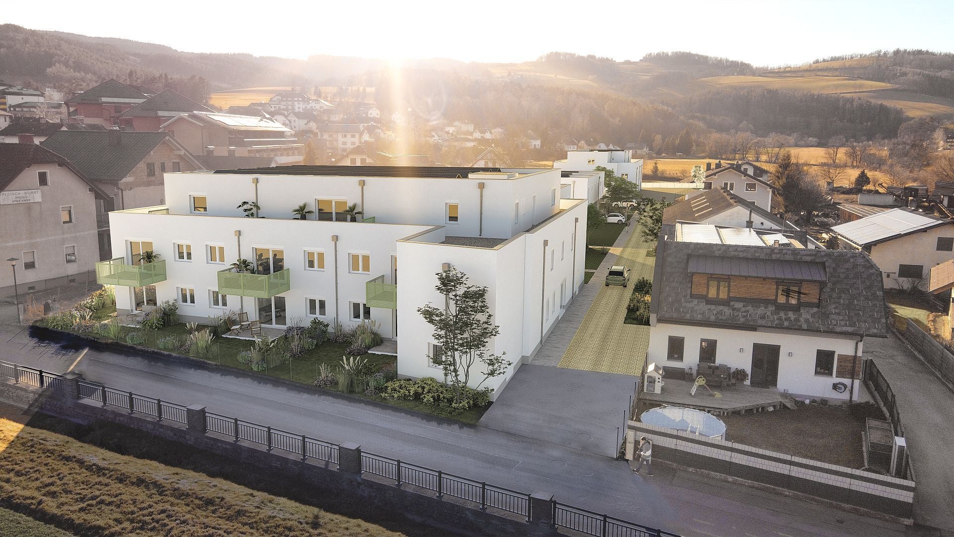 Moderne Wohnanlage mit weißen Gebäuden, grünen Balkonen und einem Einfamilienhaus daneben.