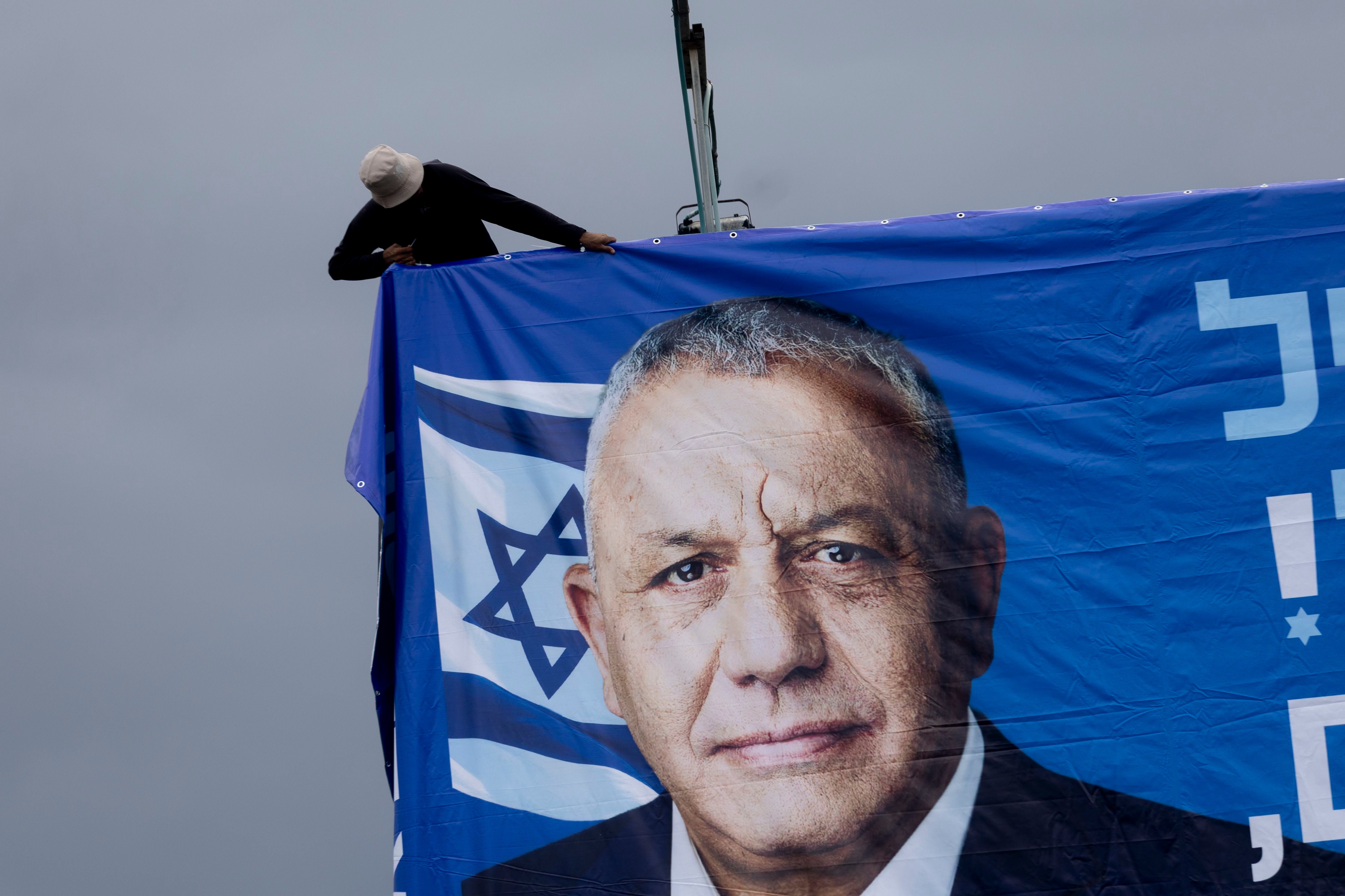 Ein Arbeiter hängt ein Wahlplakat mit Gadi Eisenkot und einer israelischen Flagge auf.