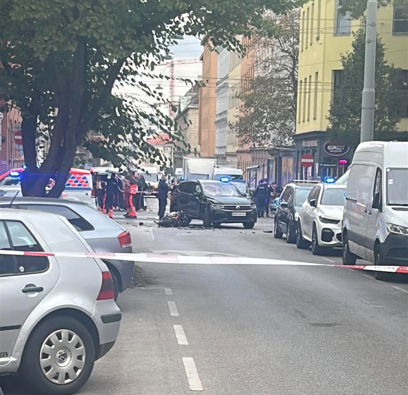 Unfallstelle mit beschädigtem Auto und Motorrad, Polizei und Rettungskräften am Einsatzort.