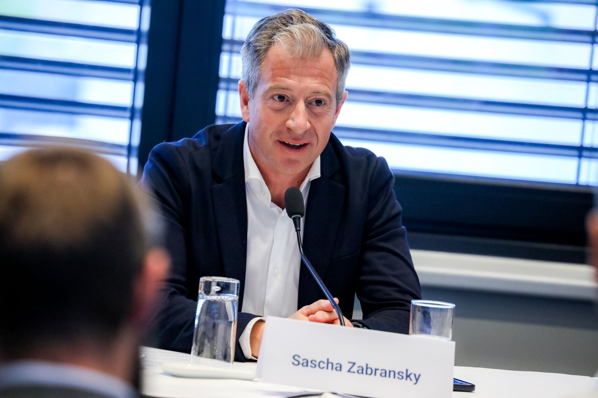 Ein Mann spricht bei einer Konferenz, vor ihm steht ein Namensschild "Sascha Zabransky".
