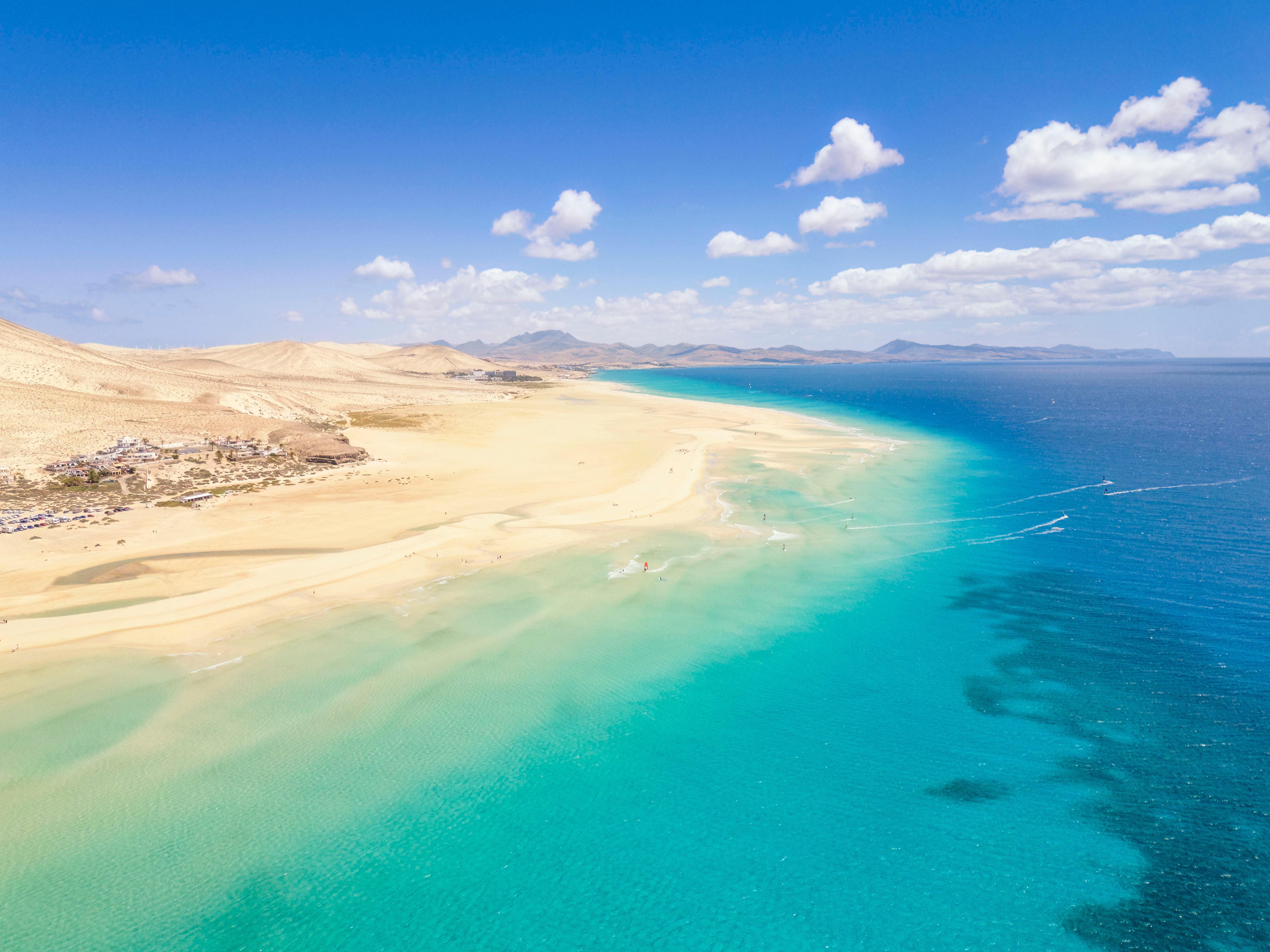 Weißer Sandstrand mit türkisblauem Meer und wenigen Wolken am Himmel, Blick aus der Luft.