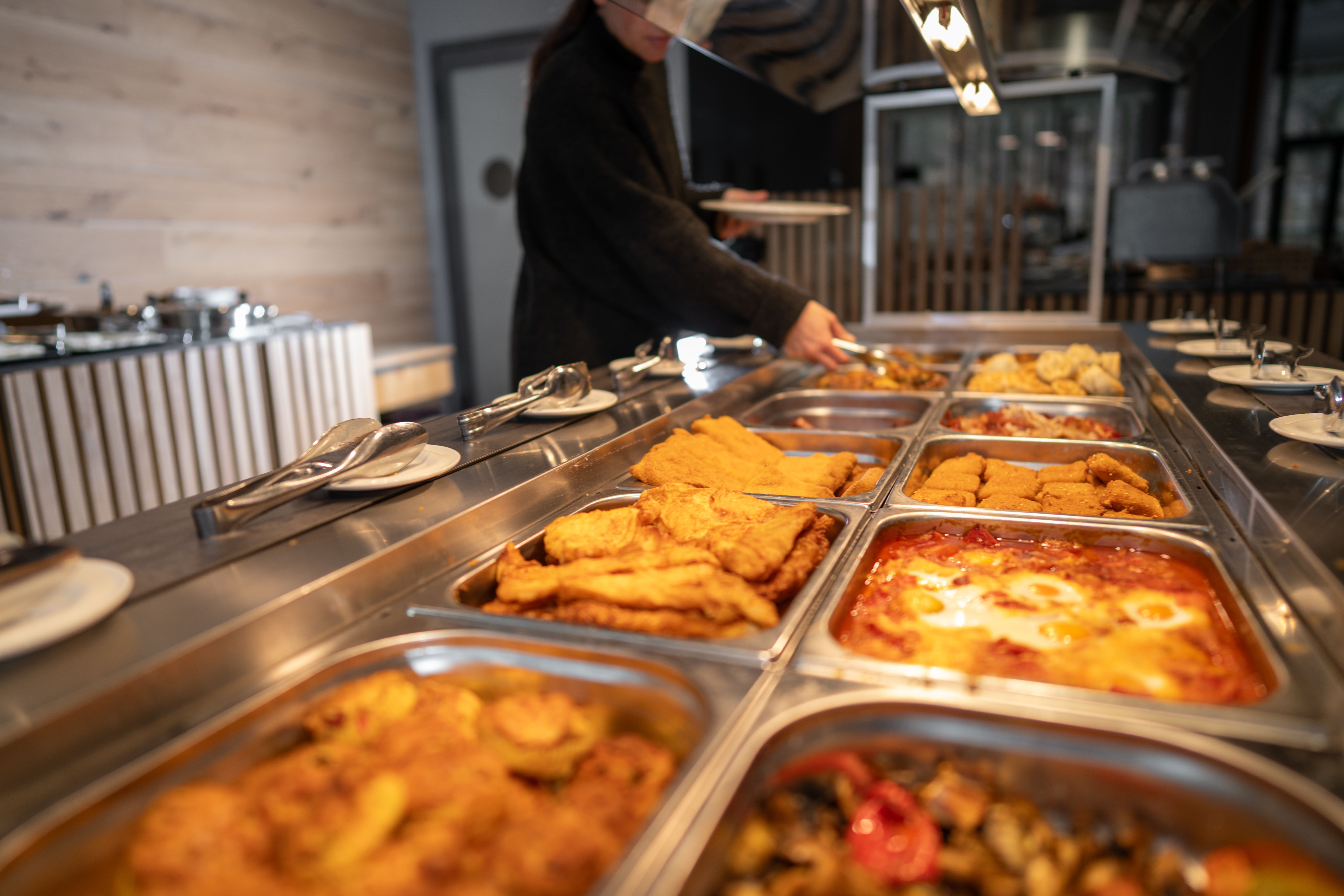 Frau bedient sich an einem Buffet mit verschiedenen warmen Gerichten im Hotelrestaurant.