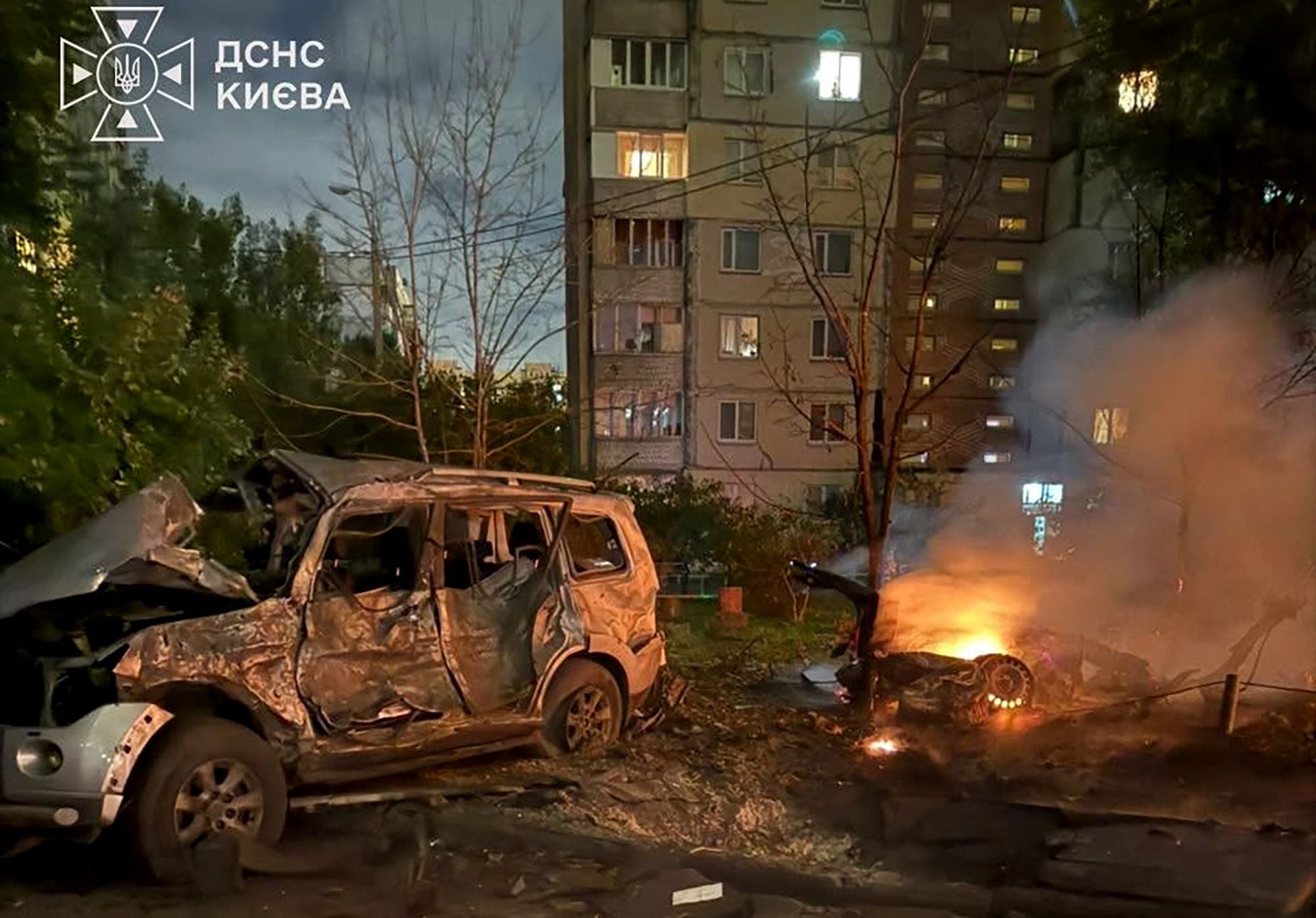 Zerstörte und brennende Autos vor einem beschädigten Wohnhaus bei Nacht in Kiew.