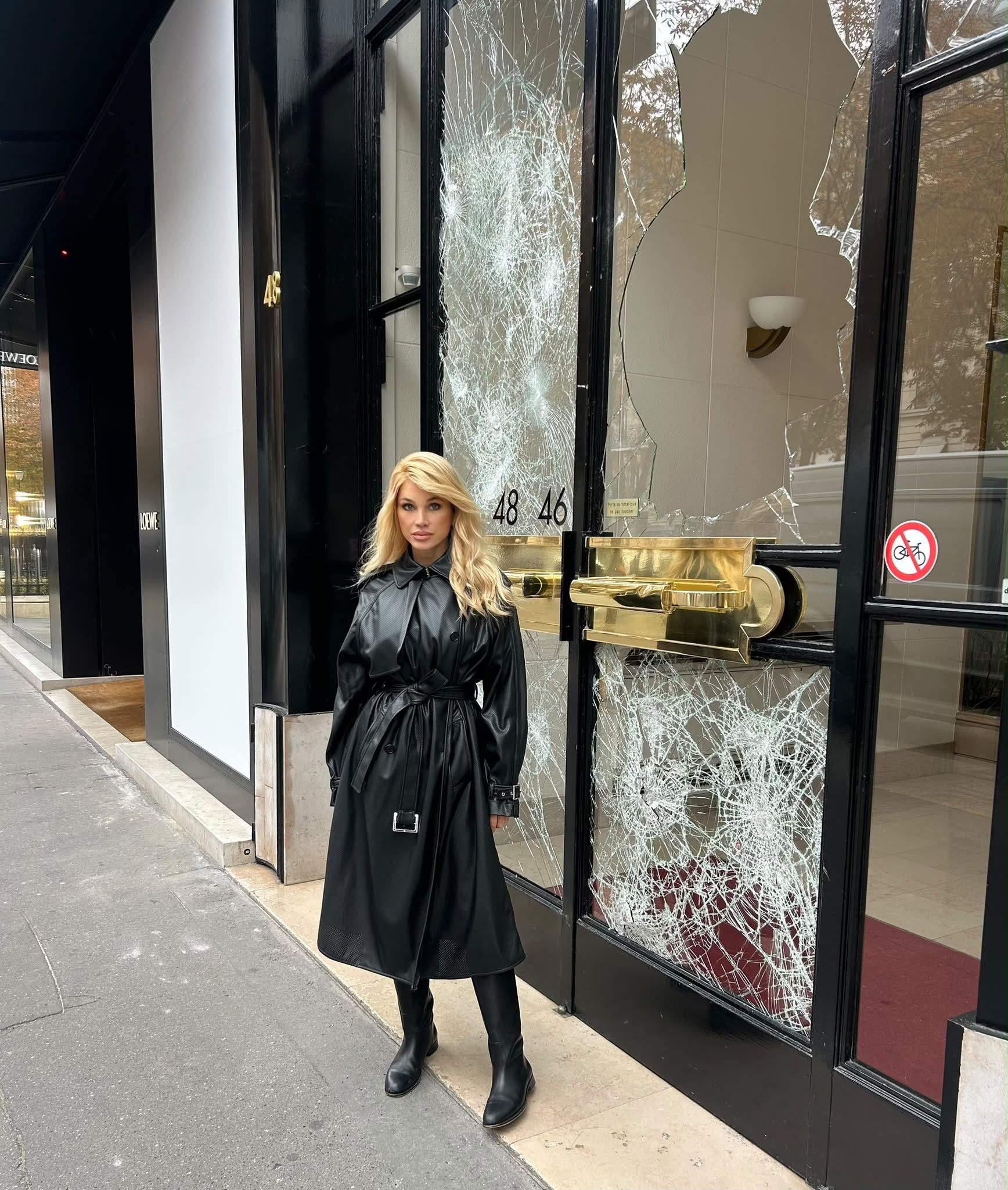 Frau in schwarzem Mantel steht vor einer Tür mit zerbrochenen Glasscheiben in Paris.