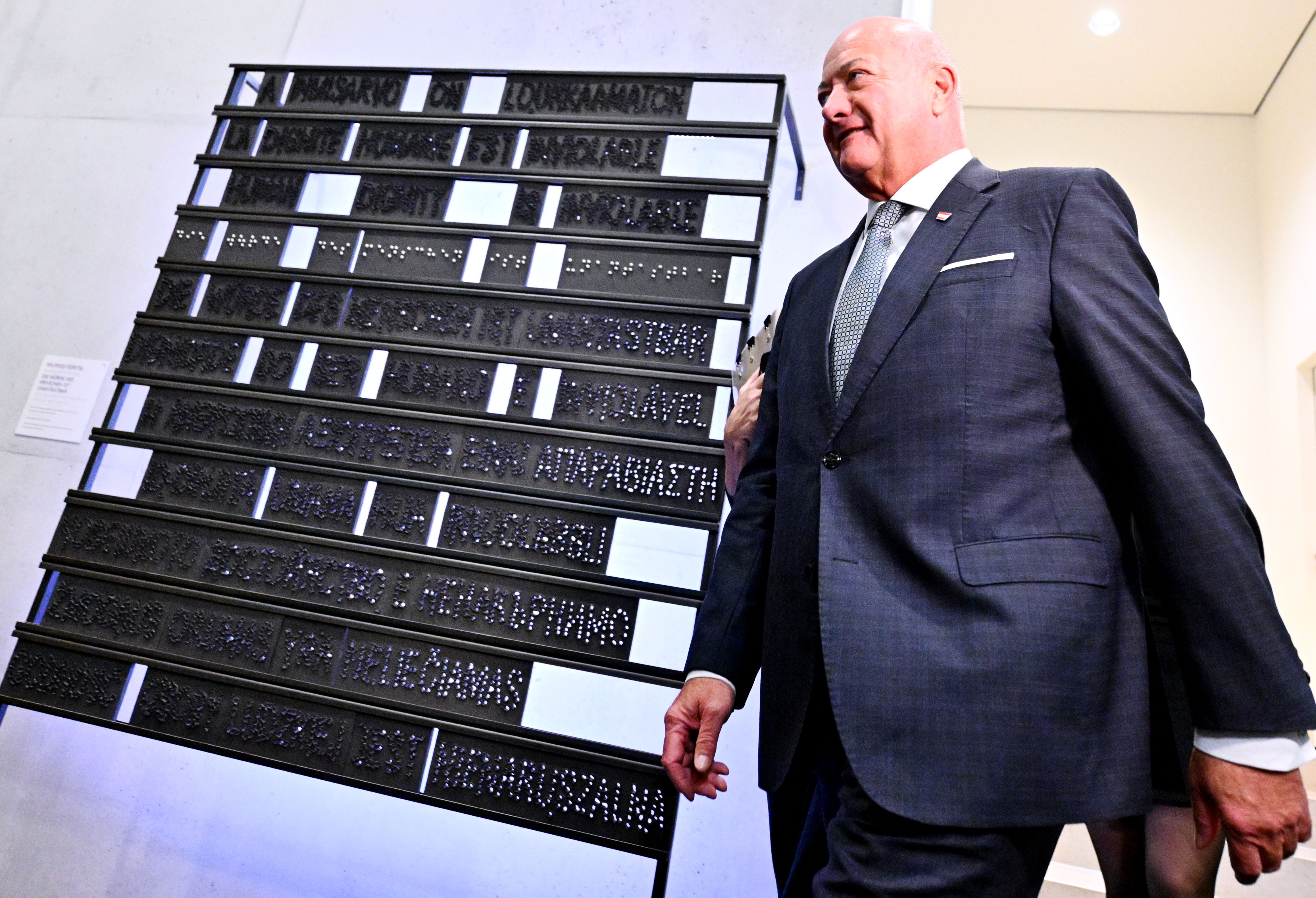 Ein Mann im Anzug steht vor einer Tafel mit Blindenschrift im modernen Gebäude.