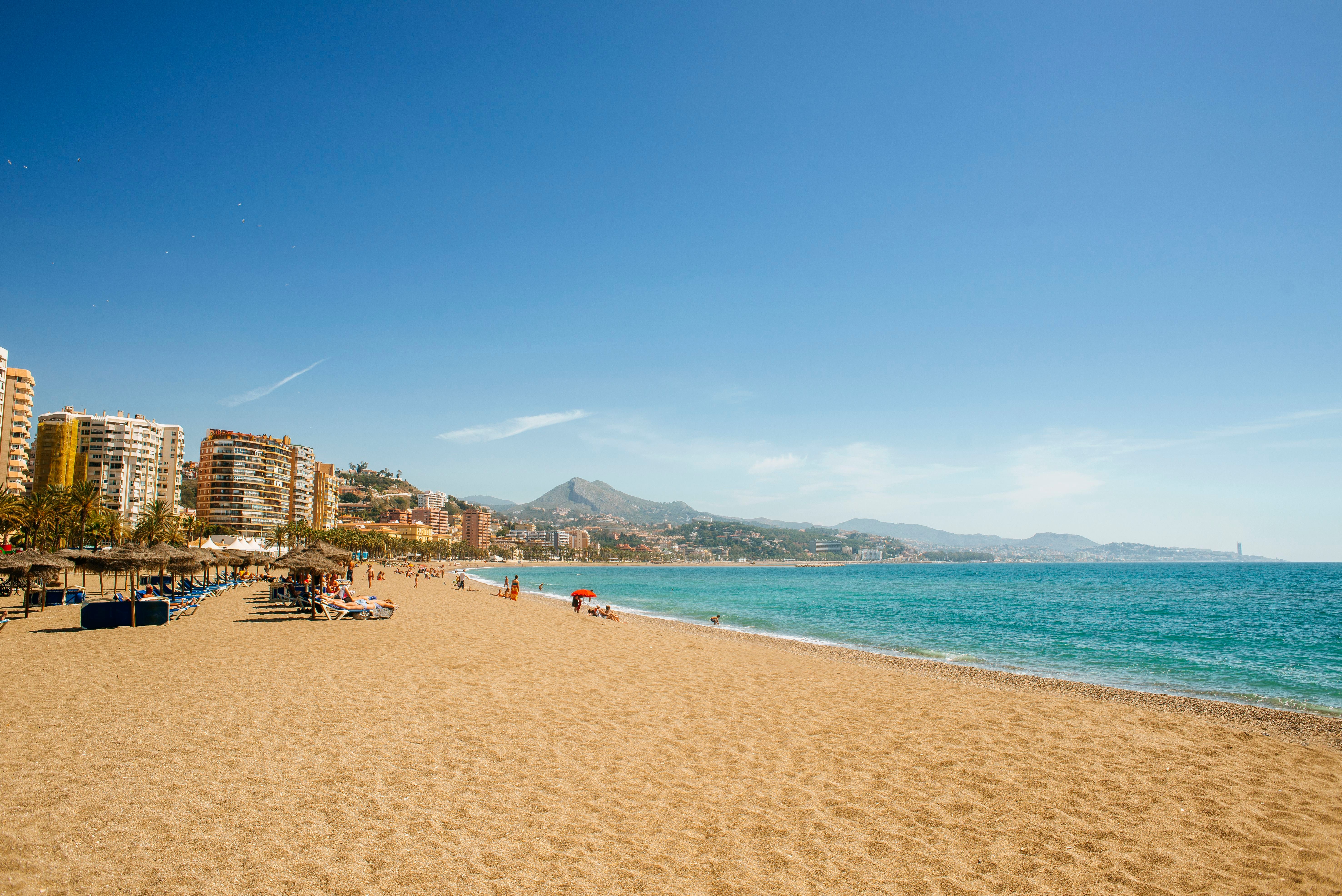Weitläufiger Sandstrand La Malagueta mit Blick auf das Meer und die Stadt Malaga im Hintergrund.