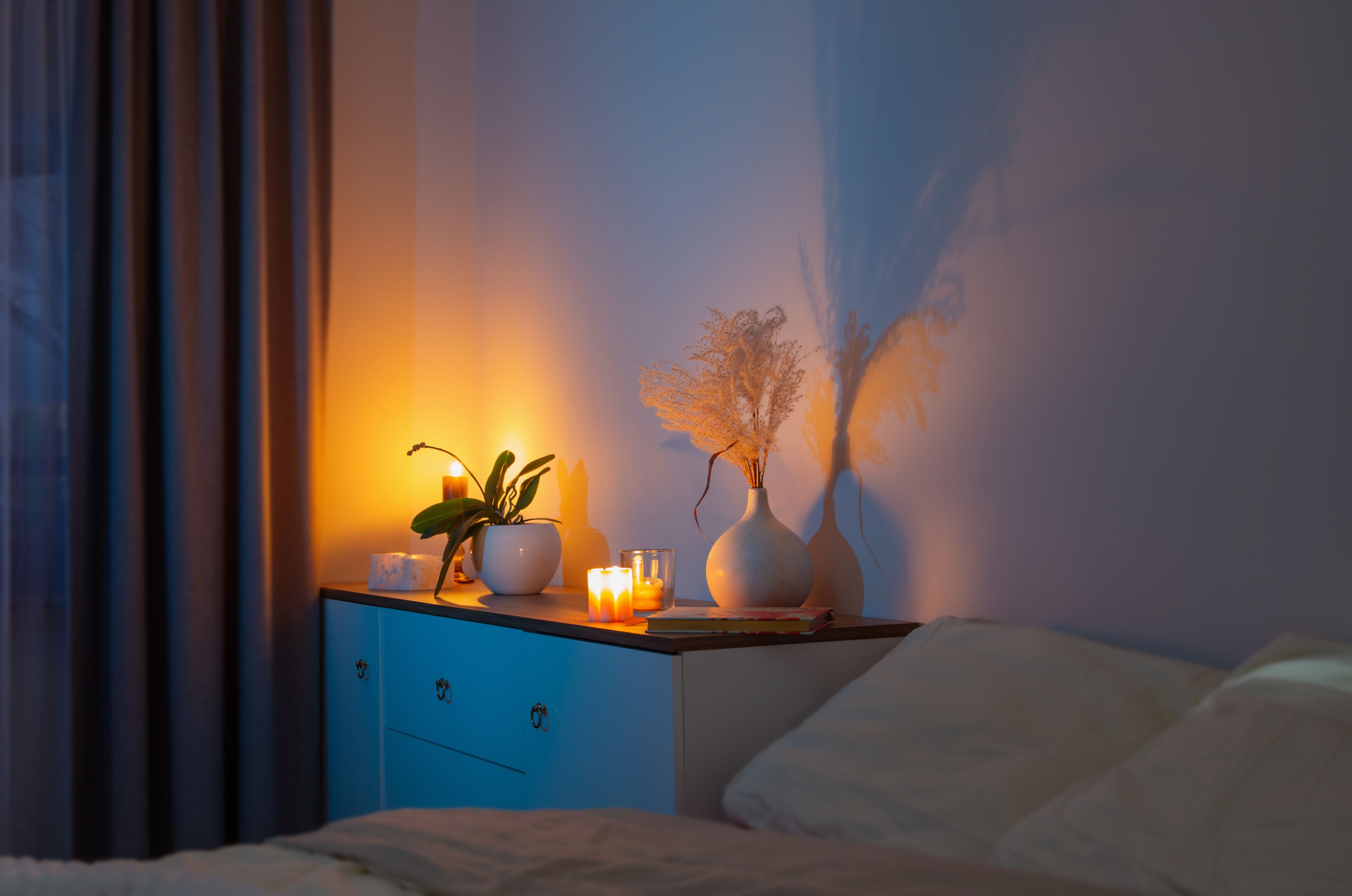 Kerzen brennen auf einer Kommode neben Blumenvasen in einem Schlafzimmer bei Nacht.