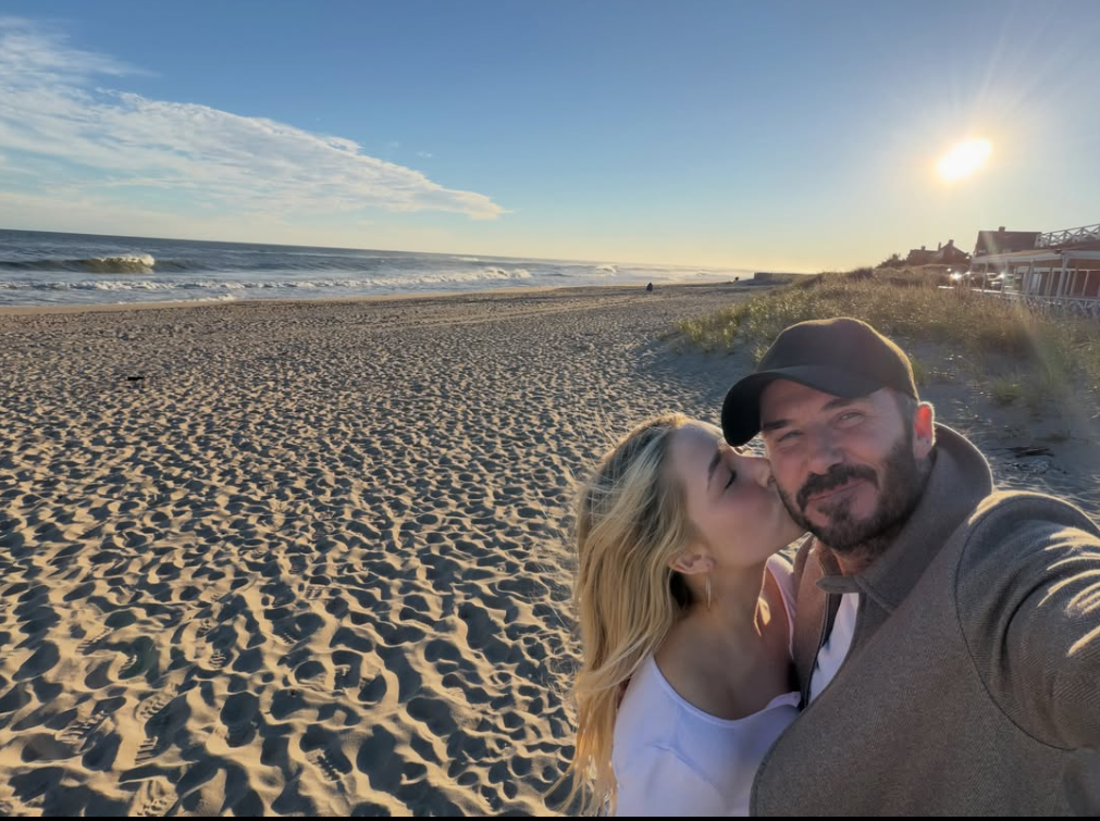 Ein Mann und ein Mädchen machen ein Selfie am Strand bei Sonnenuntergang, sie küsst ihn auf die Wange.