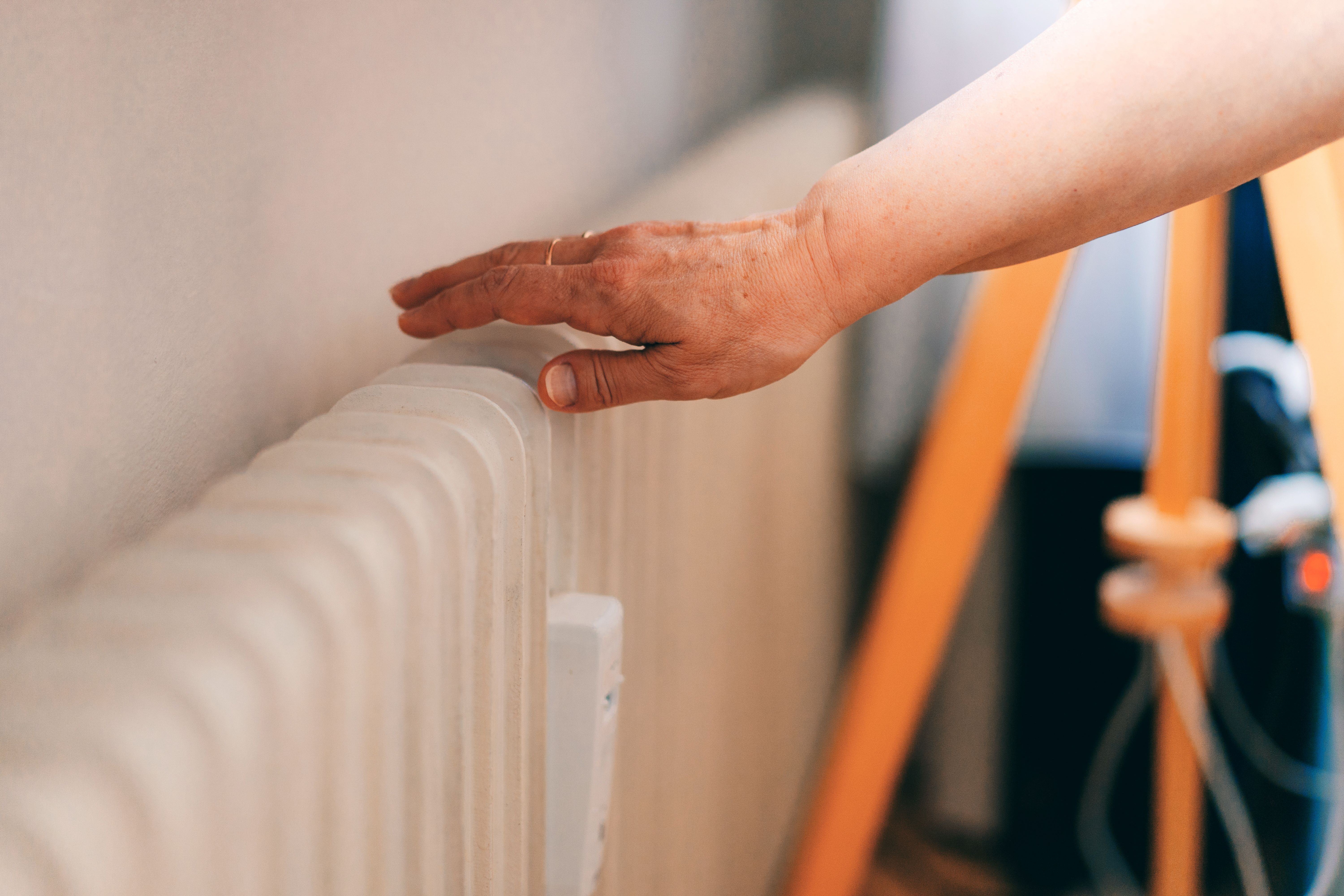 Eine Hand prüft die Temperatur eines Heizkörpers in einer Wohnung.
