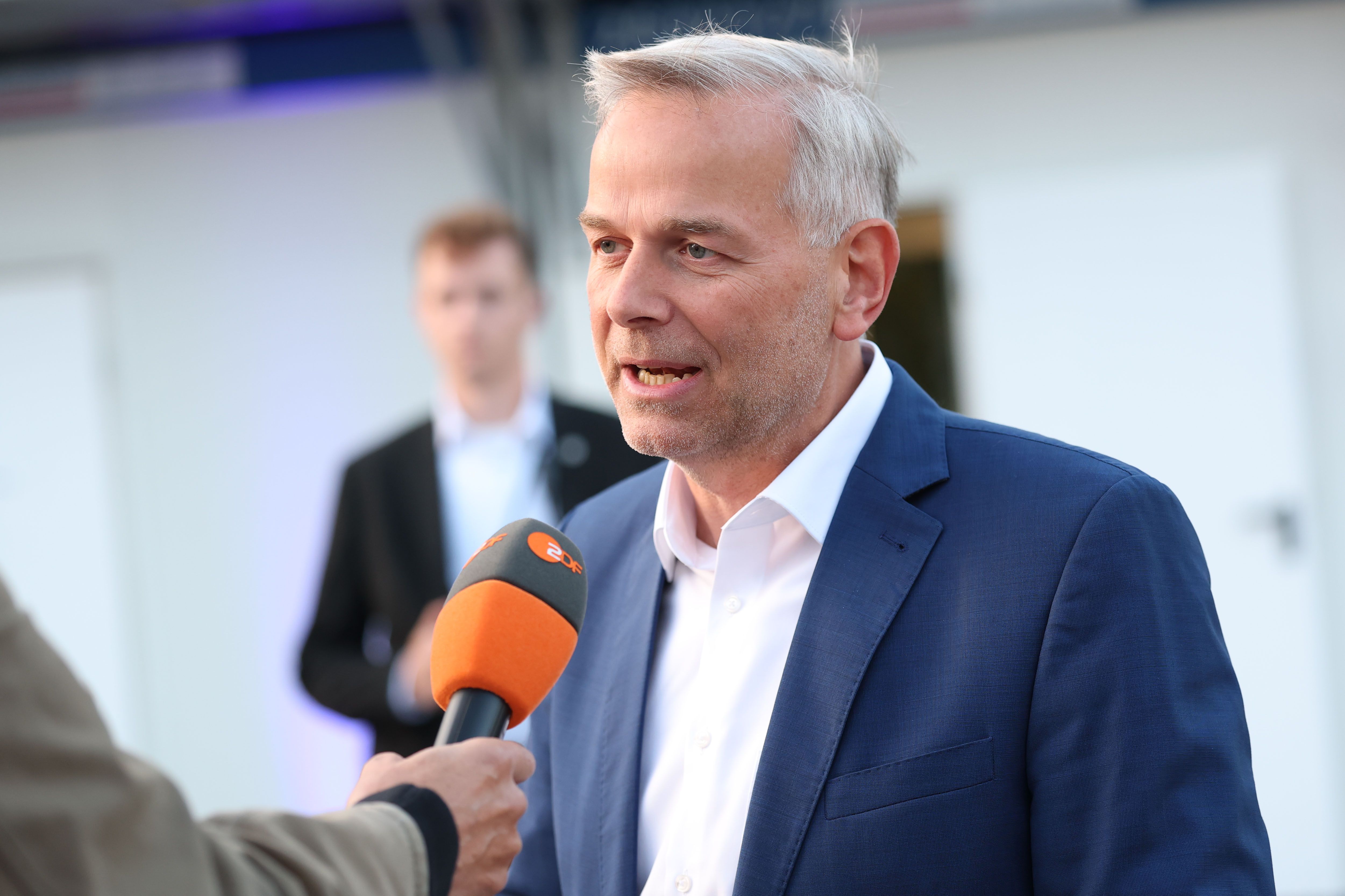 Ein Mann im blauen Anzug gibt ein Interview vor einem Mikrofon mit ZDF-Logo.