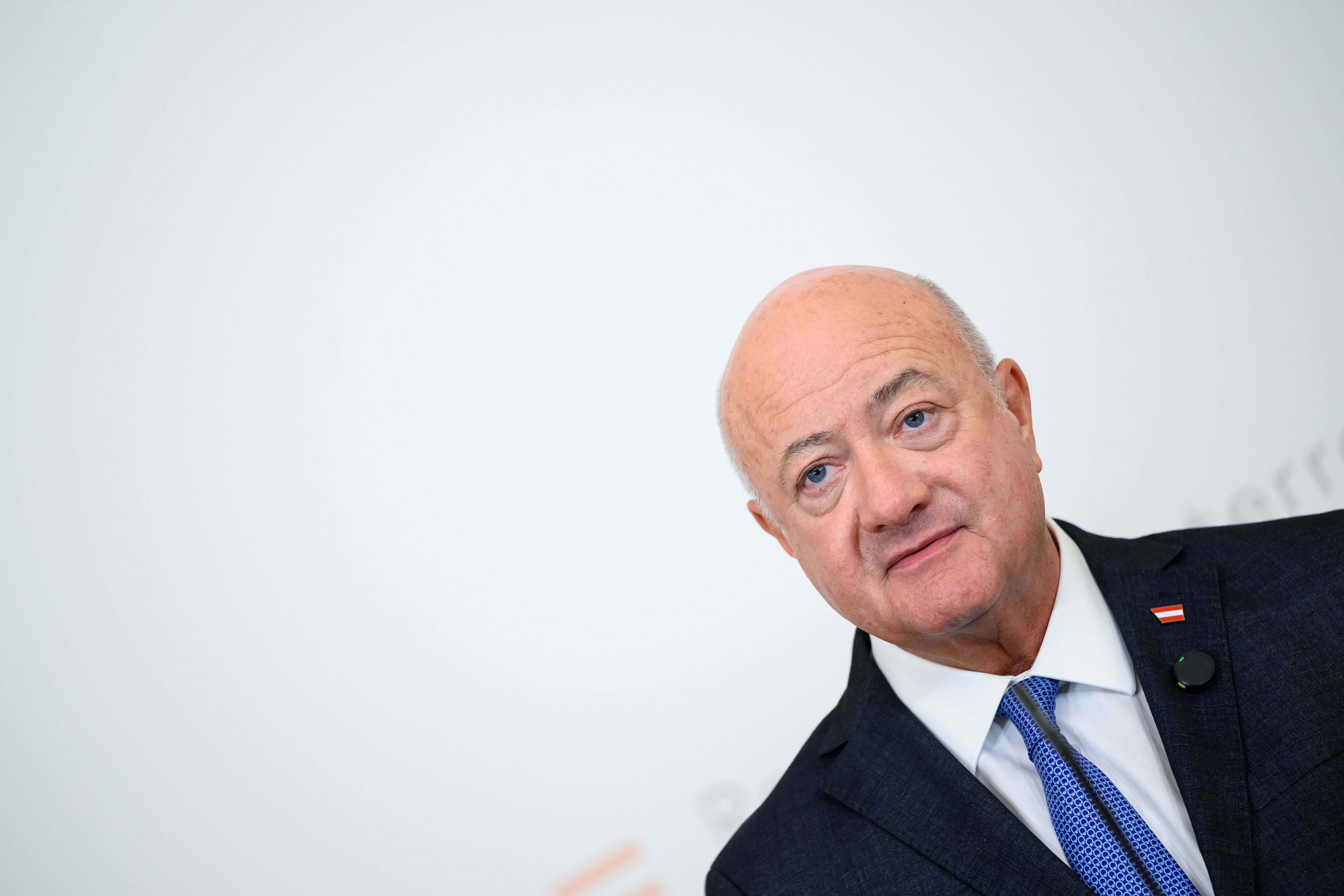 Ein Mann im Anzug mit Krawatte steht vor weißem Hintergrund und schaut leicht zur Seite.