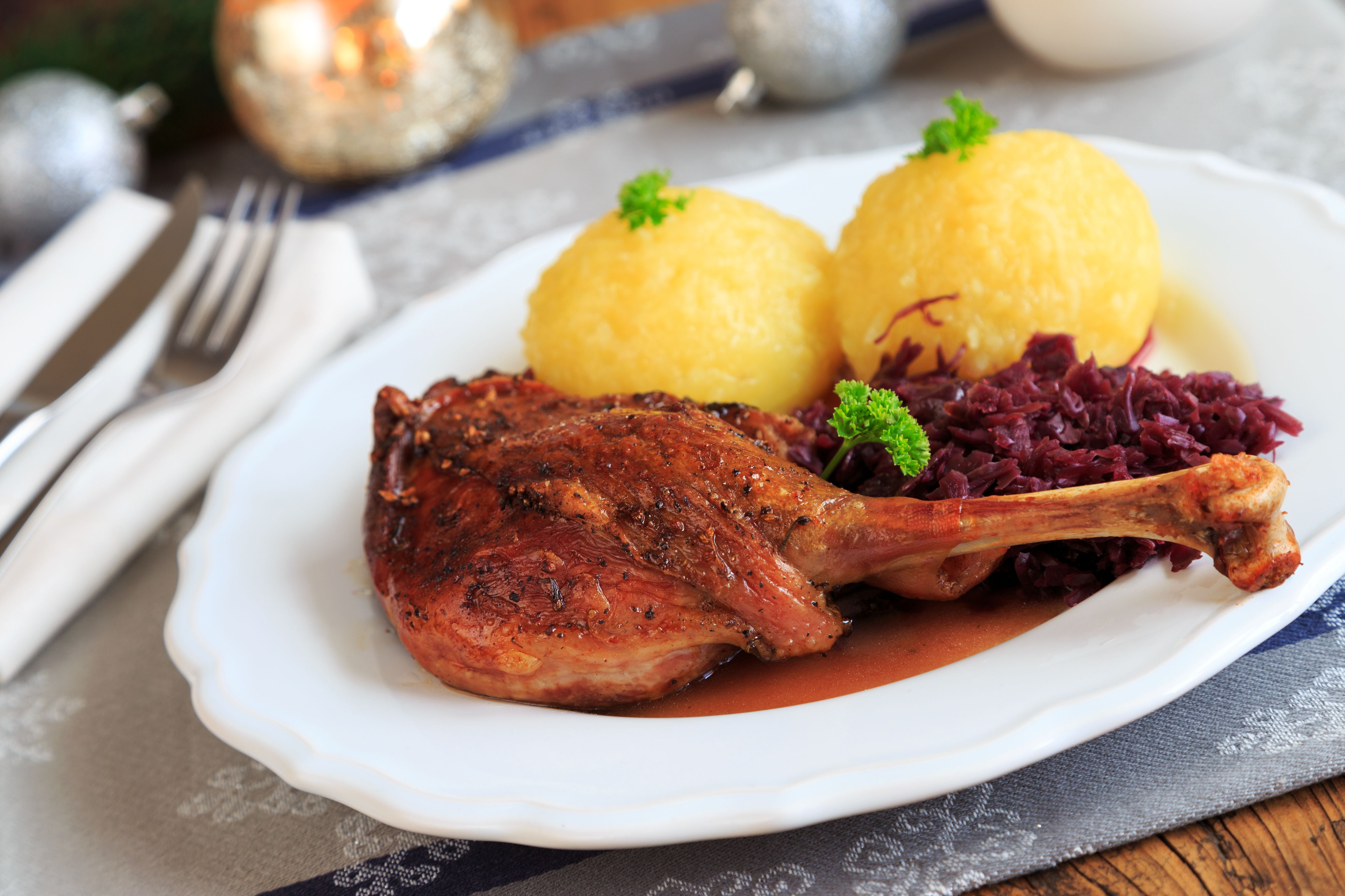 Gänsekeule mit Rotkohl und zwei Kartoffelklößen auf einem weißen Teller.