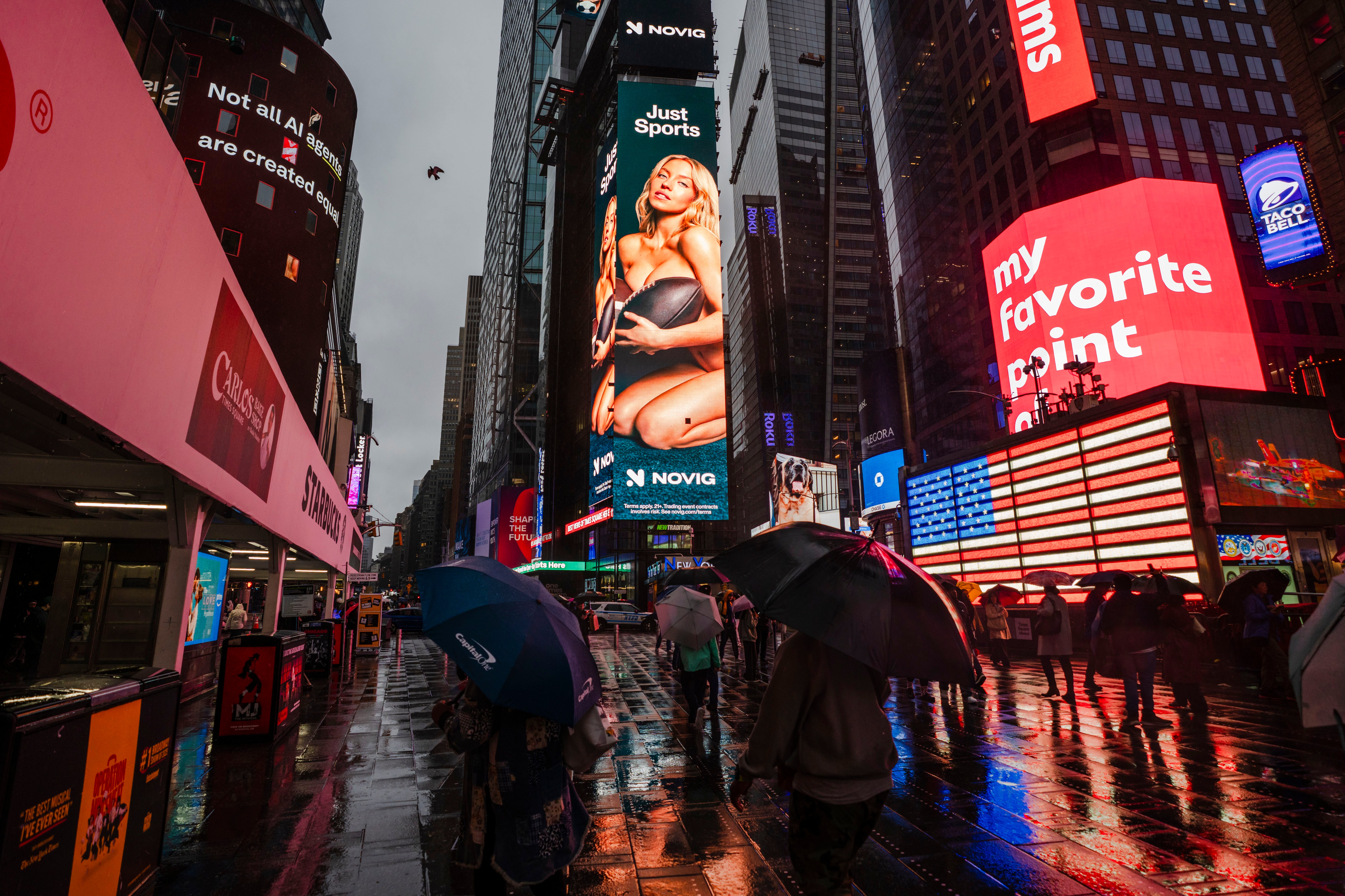 Menschen mit Regenschirmen laufen durch den nassen Times Square mit hellen Werbetafeln im Regen.