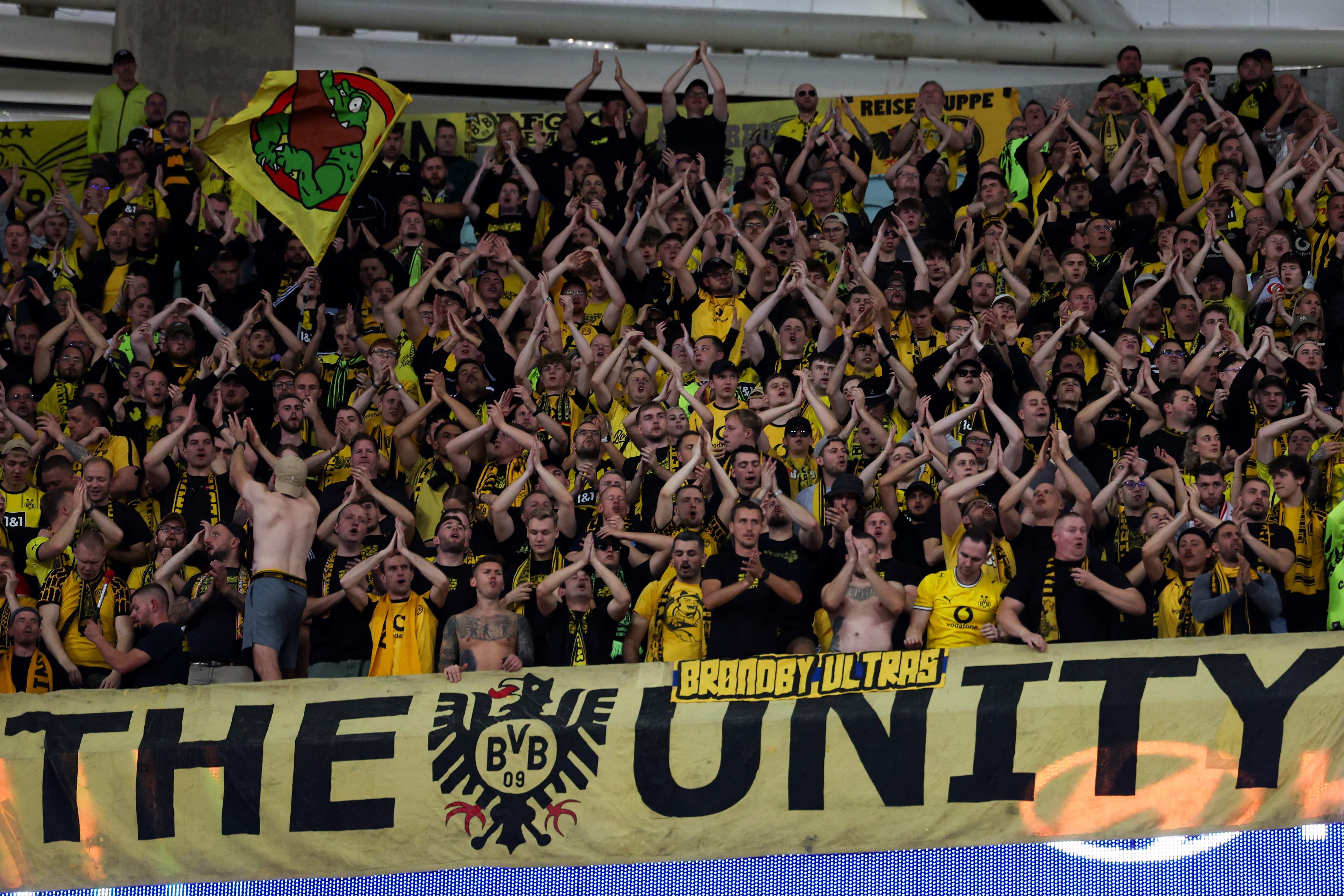 Zahlreiche Fans von Borussia Dortmund stehen dicht an dicht auf der Tribüne im Stadion und klatschen geschlossen mit erhobenen Händen.