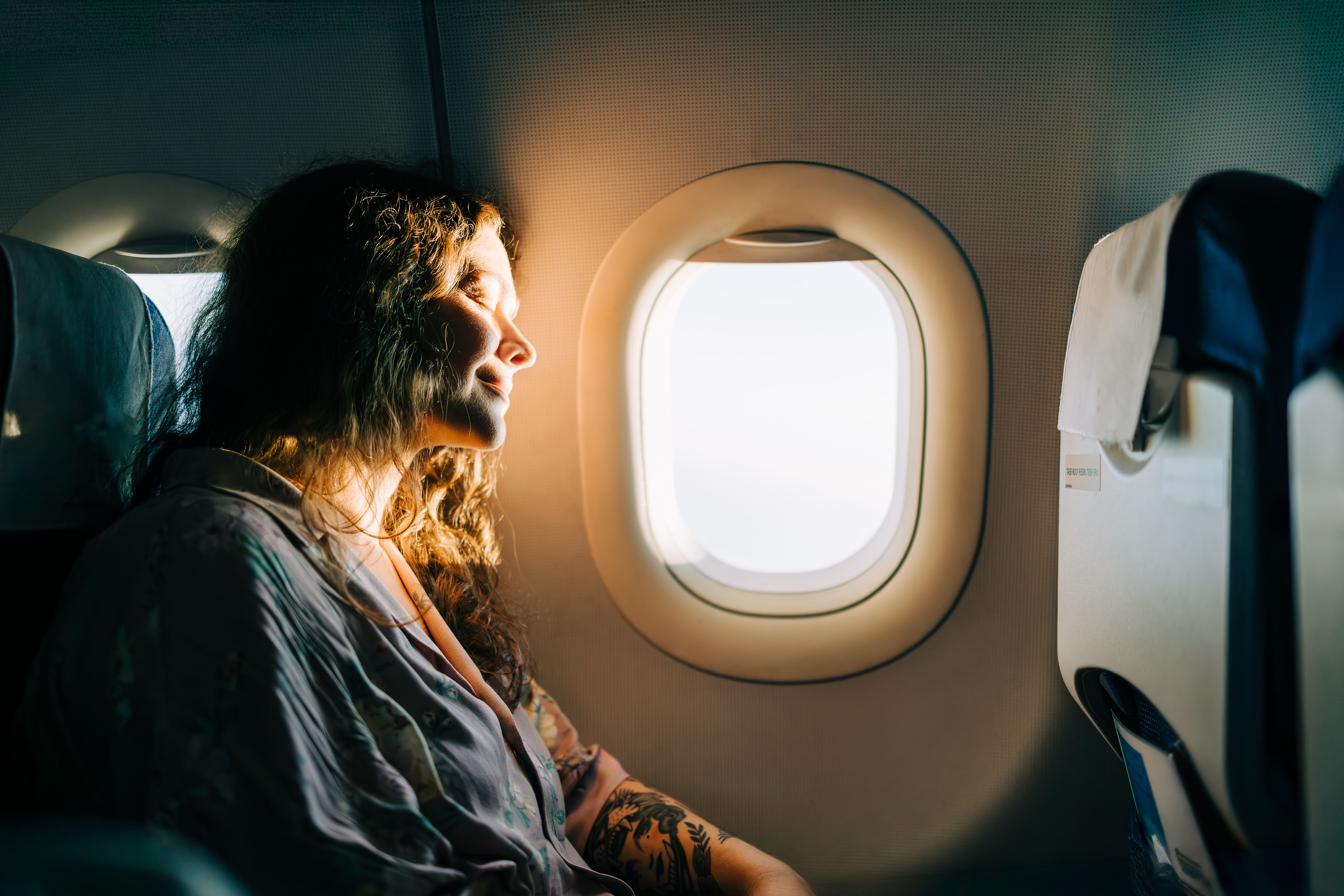 Frau genießt entspannt den Sonnenschein am Fensterplatz im Flugzeug.
