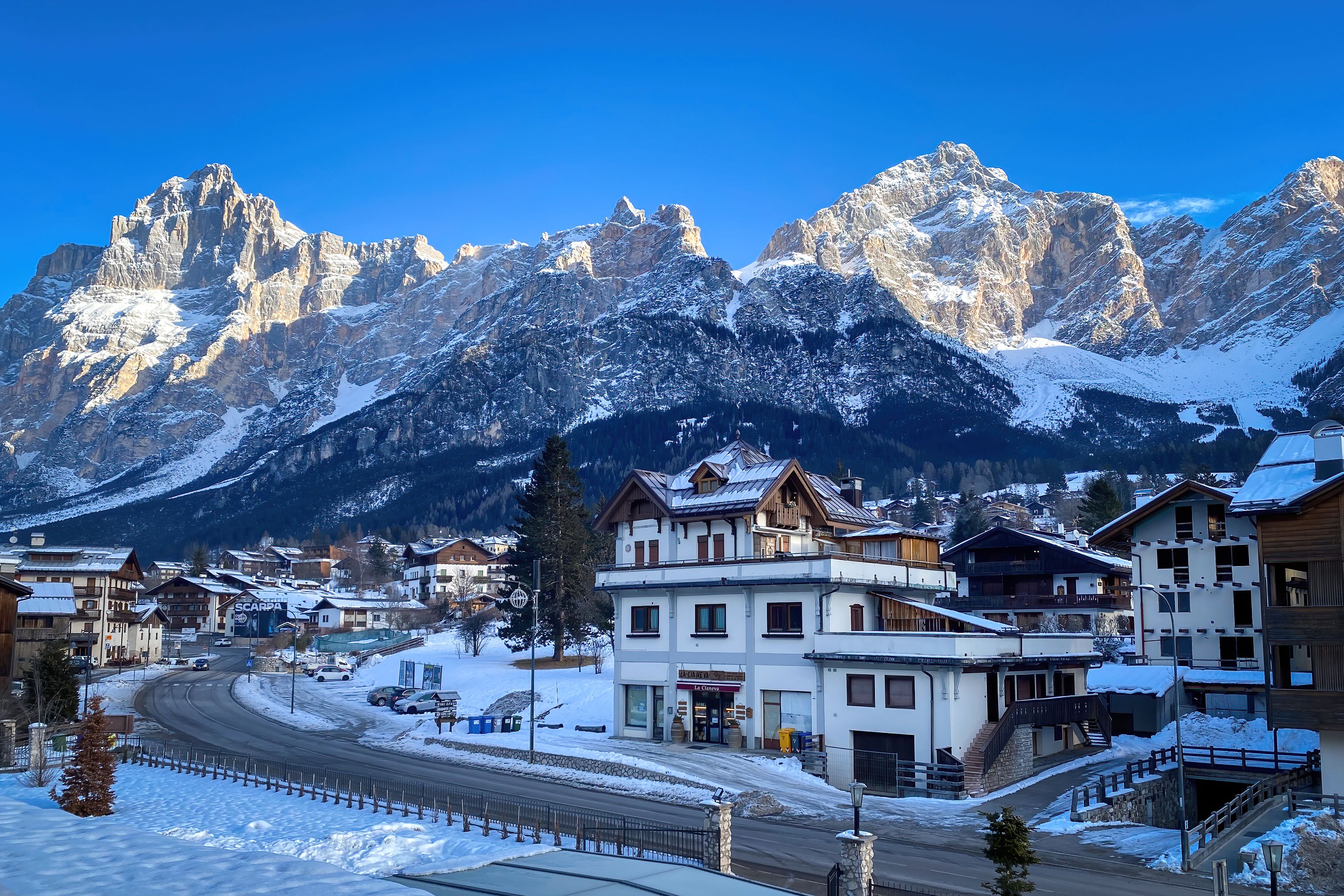 Winterliche Stadt San Vito di Cadore vor schneebedeckten Dolomiten und blauem Himmel.