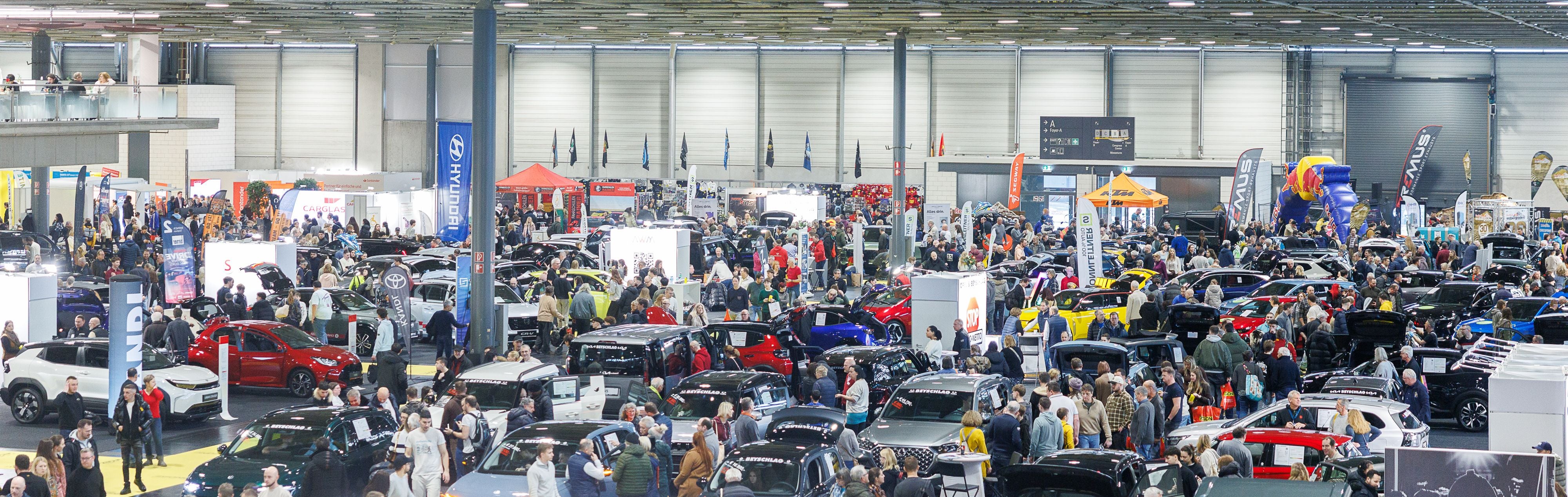Viele Menschen besuchen eine Automesse mit zahlreichen ausgestellten Autos in einer Messehalle.