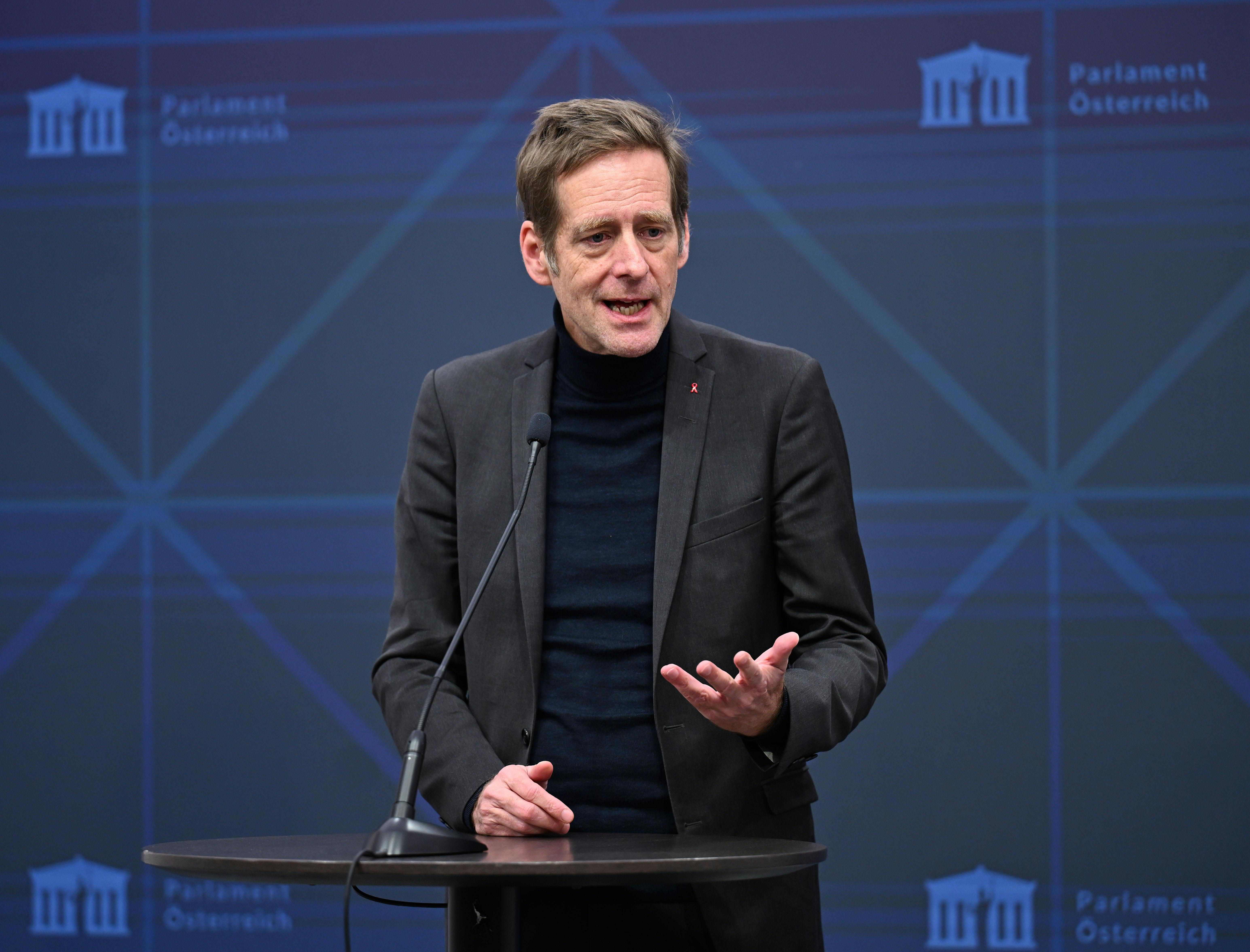 Ein Mann spricht stehend am Rednerpult vor blauem Hintergrund im österreichischen Parlament.