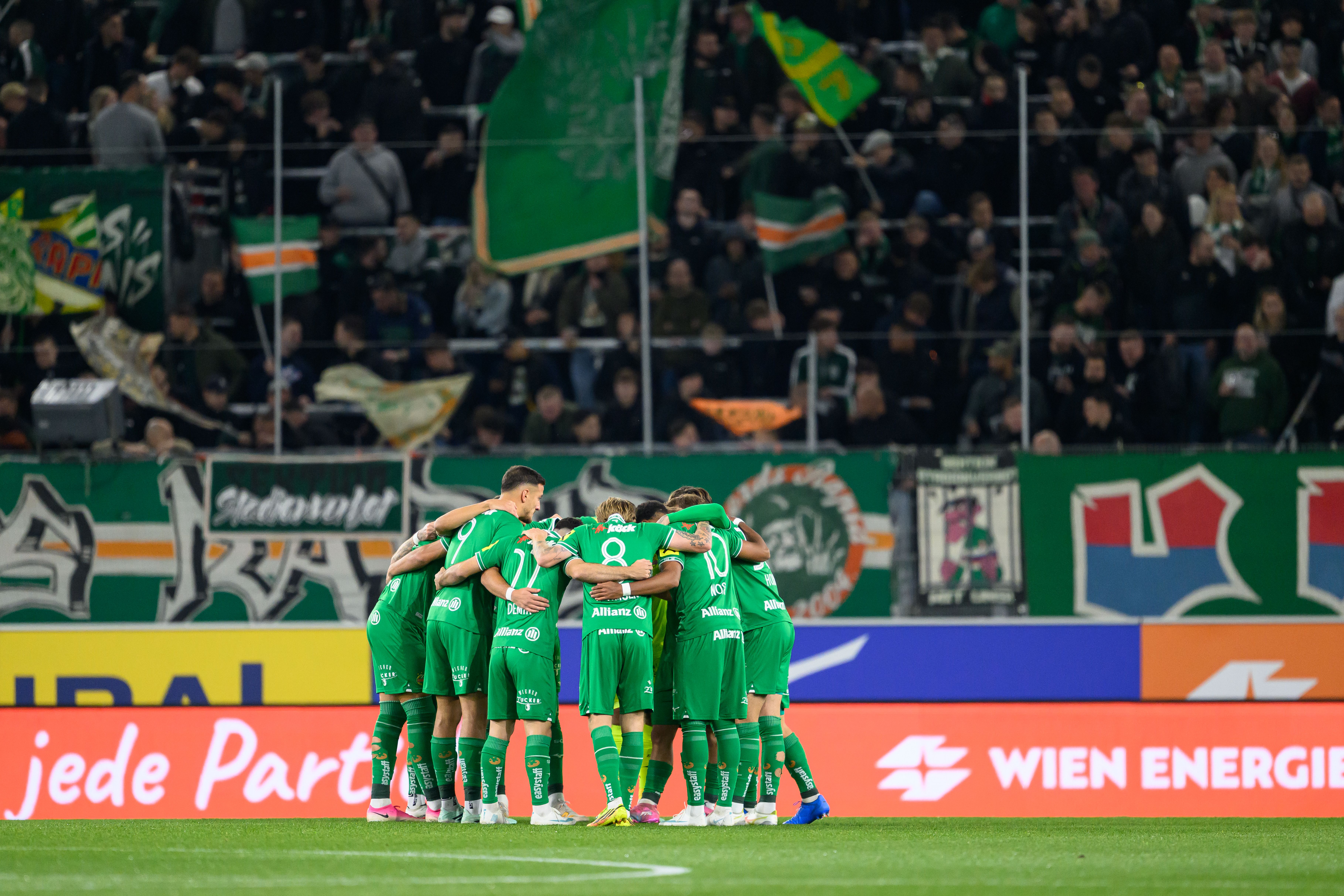 Die Mannschaft des SK Rapid stellt sich vor dem Anpfiff in grünen Trikots eng im Kreis auf dem Spielfeld zusammen.