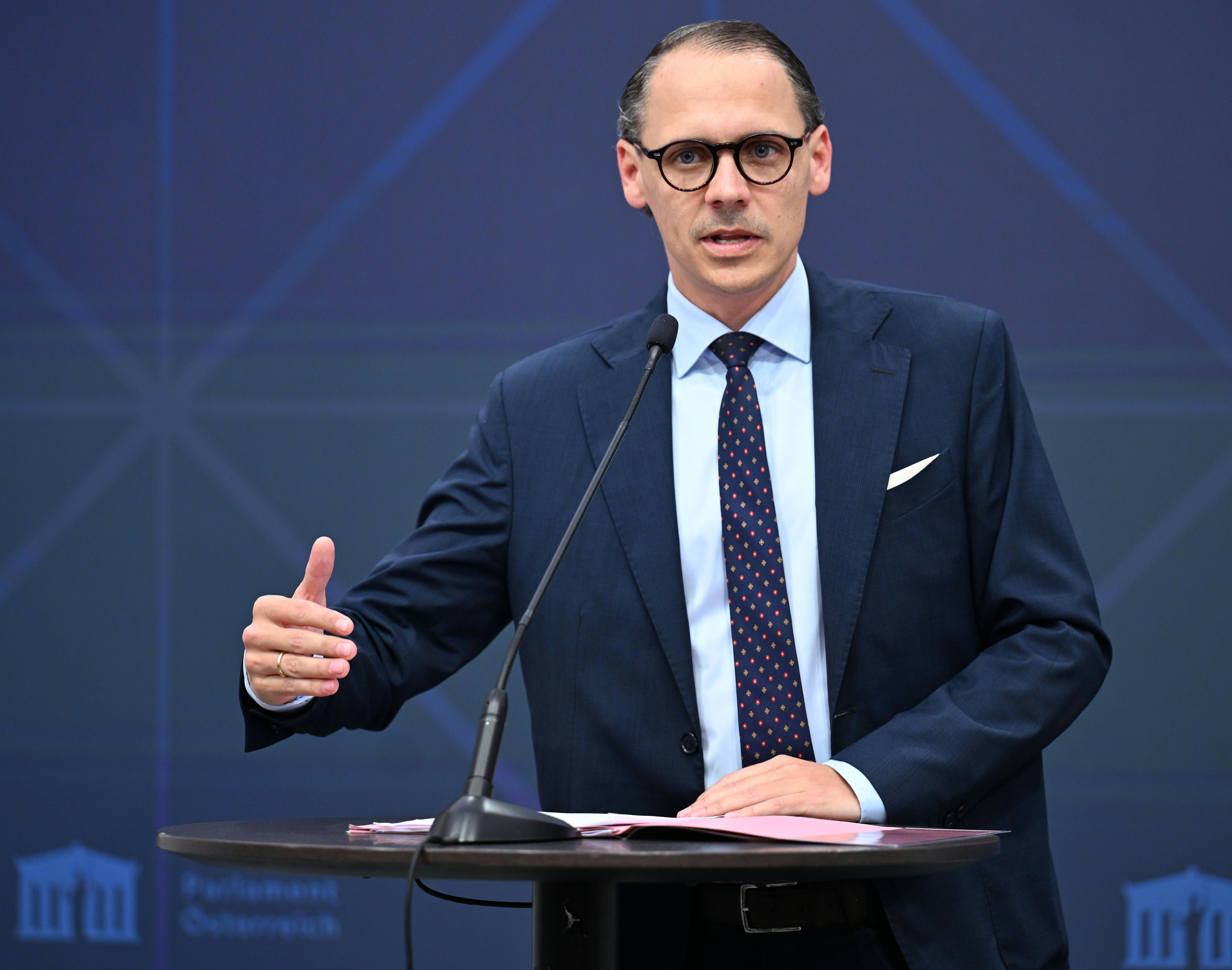 Mann im Anzug spricht an einem Rednerpult mit Mikrofon vor blauem Hintergrund.
