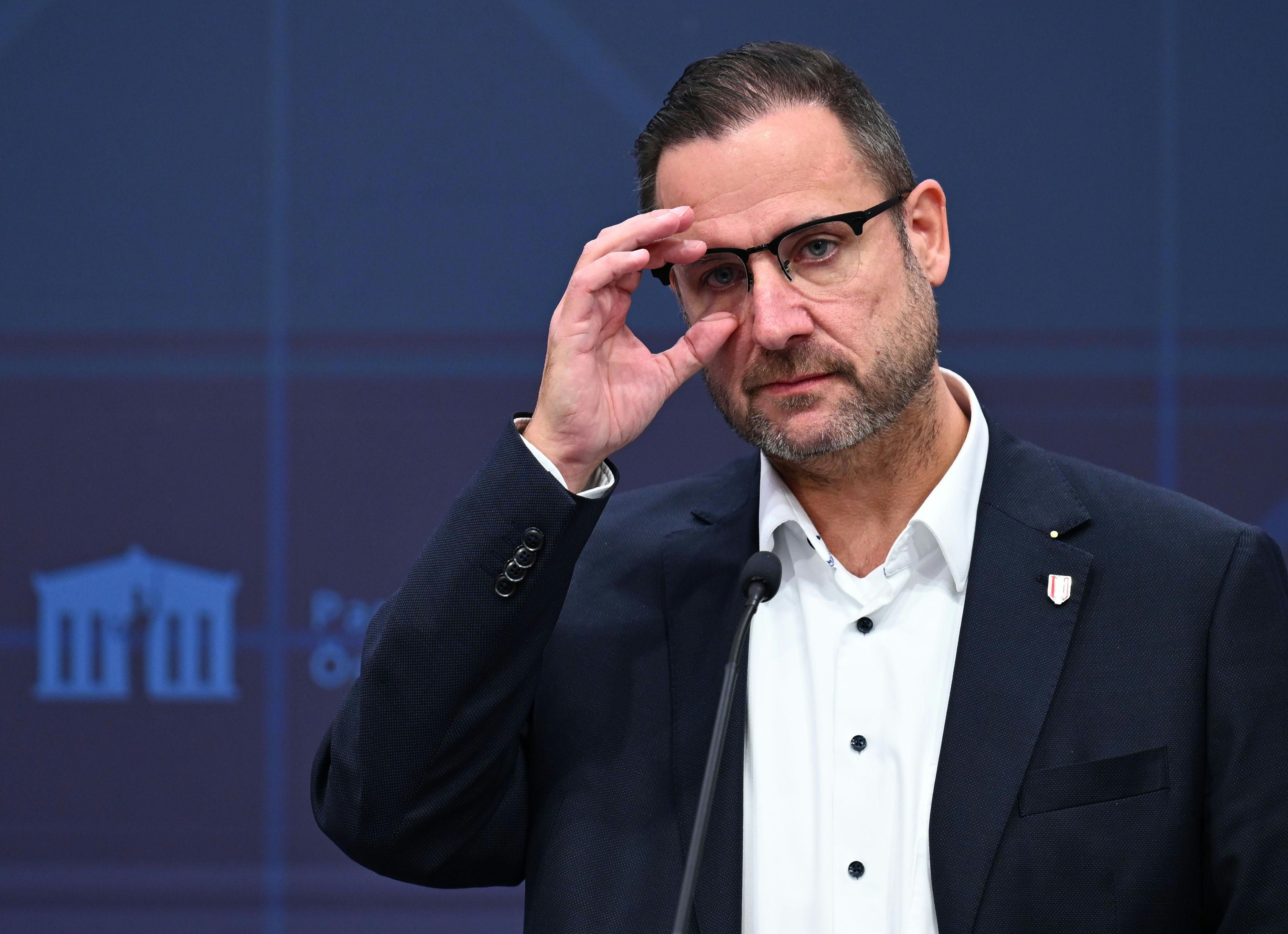 Ein Mann mit Brille steht nachdenklich an einem Rednerpult vor blauem Hintergrund.