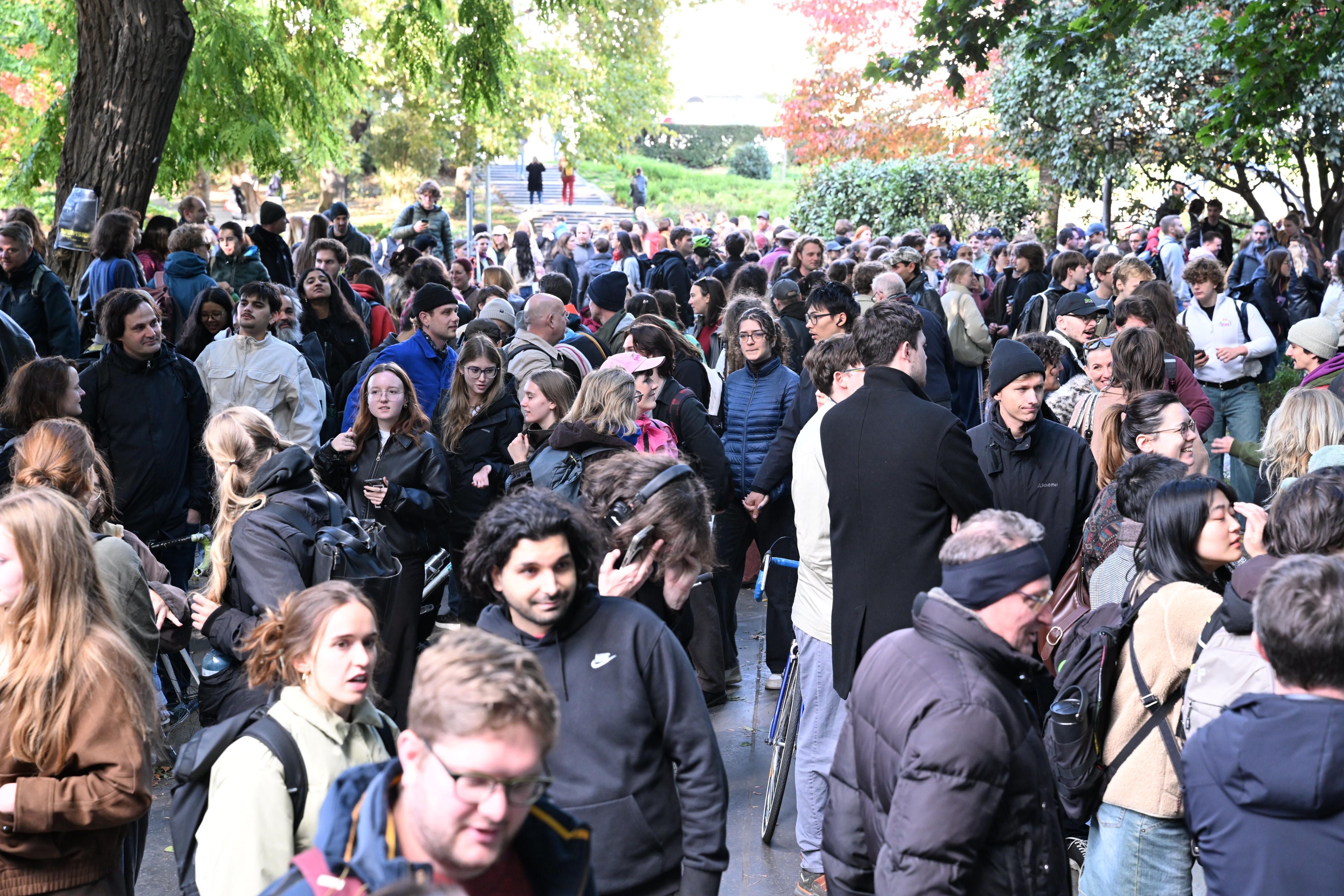 Viele Menschen versammeln sich bei einer Demo im Freien, umgeben von Bäumen und buntem Laub.