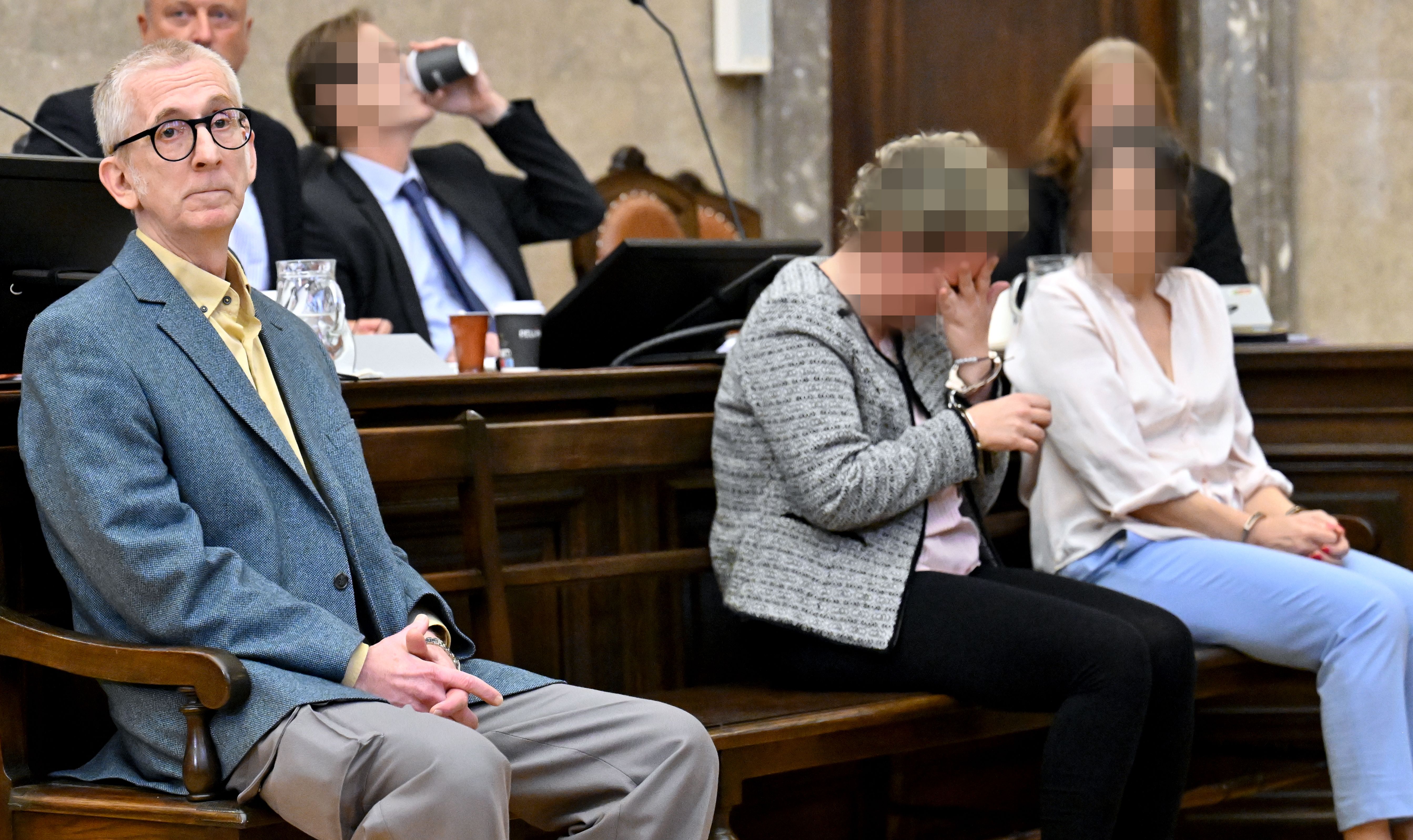 Ein Mann und zwei Frauen sitzen im Gerichtssaal, zwei Gesichter sind verpixelt.