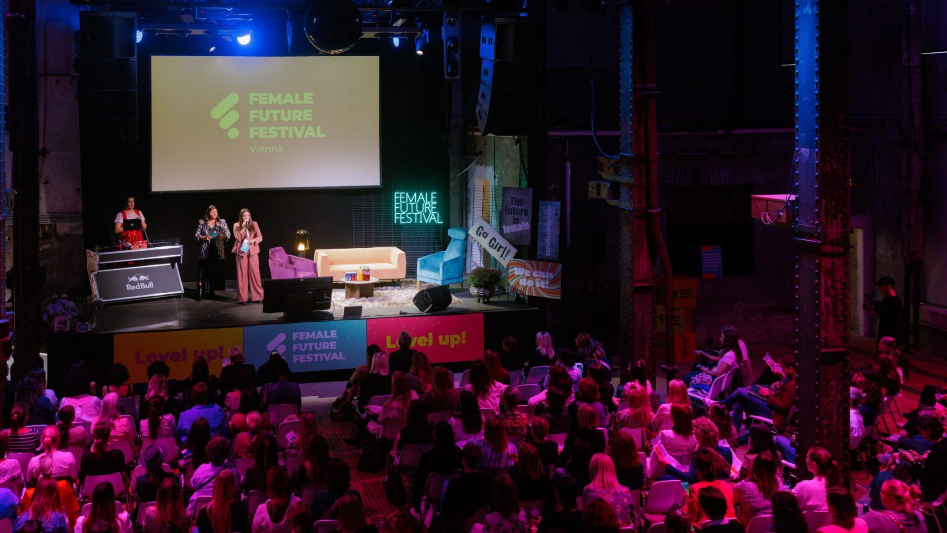 Blick auf eine Bühne beim Female Future Festival mit drei Sprecherinnen und Publikum im Saal.
