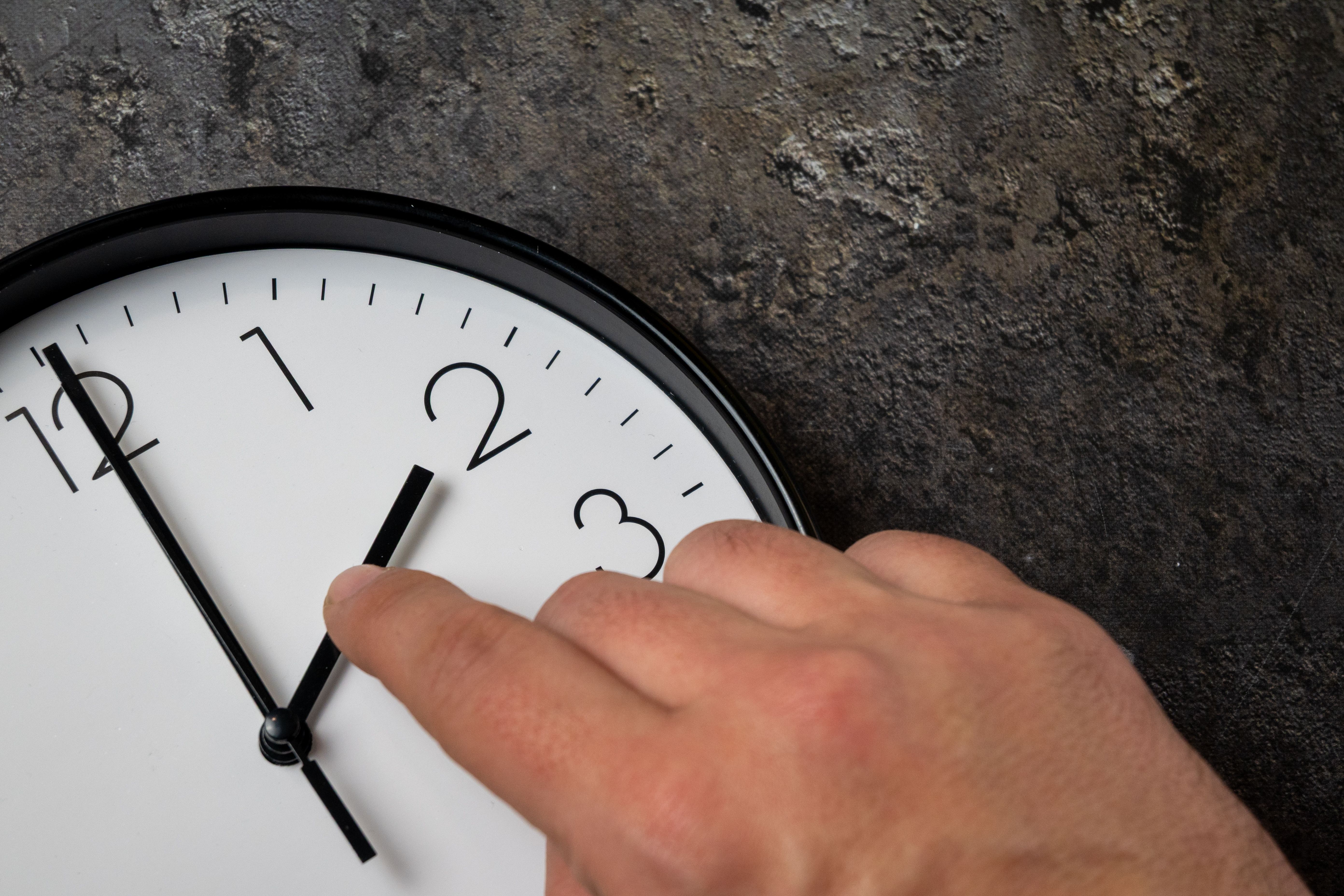 Hand stellt eine Wanduhr um, symbolisiert Umstellung auf Sommer- oder Winterzeit.