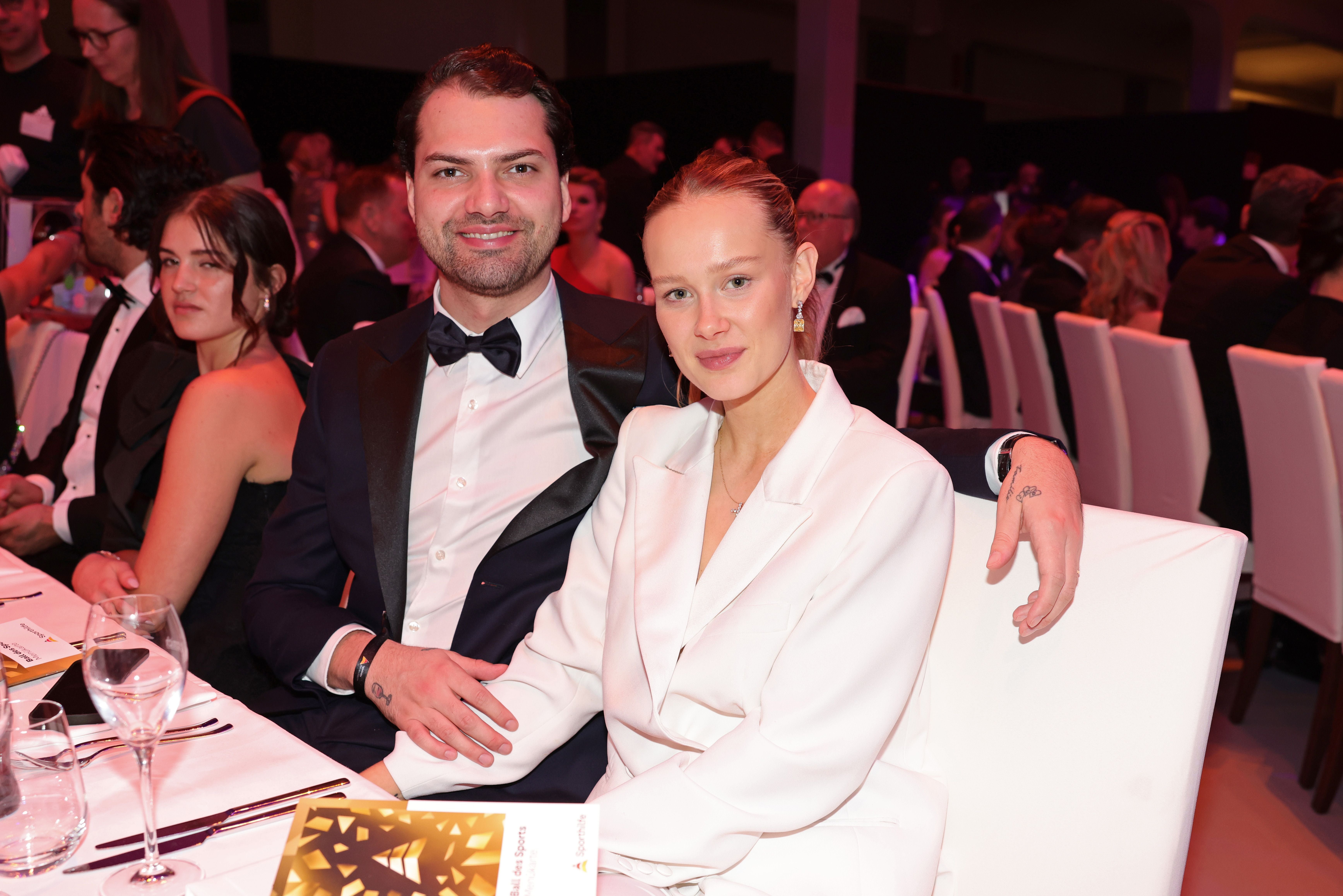 Ein elegant gekleidetes Paar sitzt bei einer Gala an einem festlich gedeckten Tisch.
