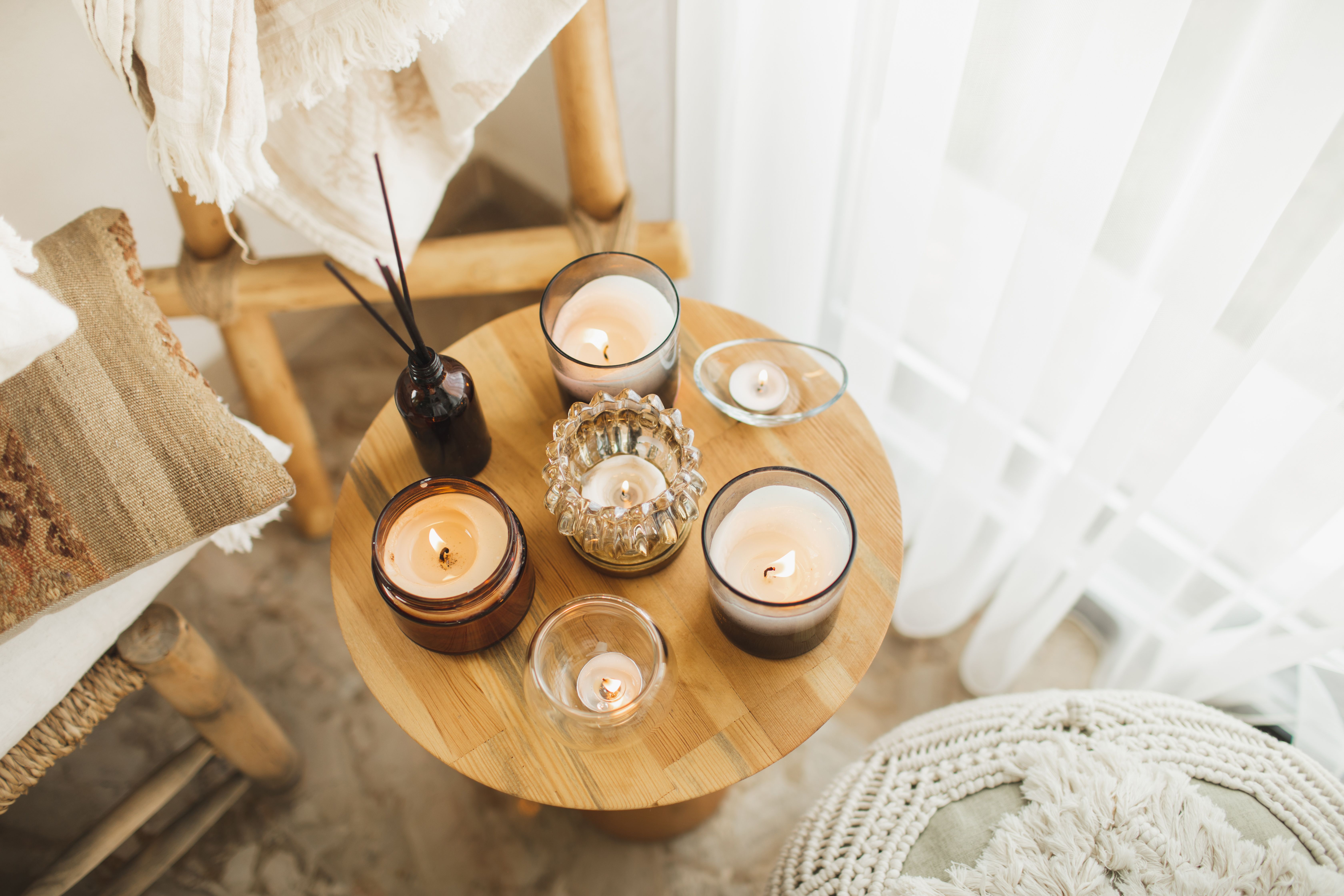 Runder Holztisch mit brennenden Kerzen, Duftstäbchen und Boho-Dekoration in gemütlicher Ecke.