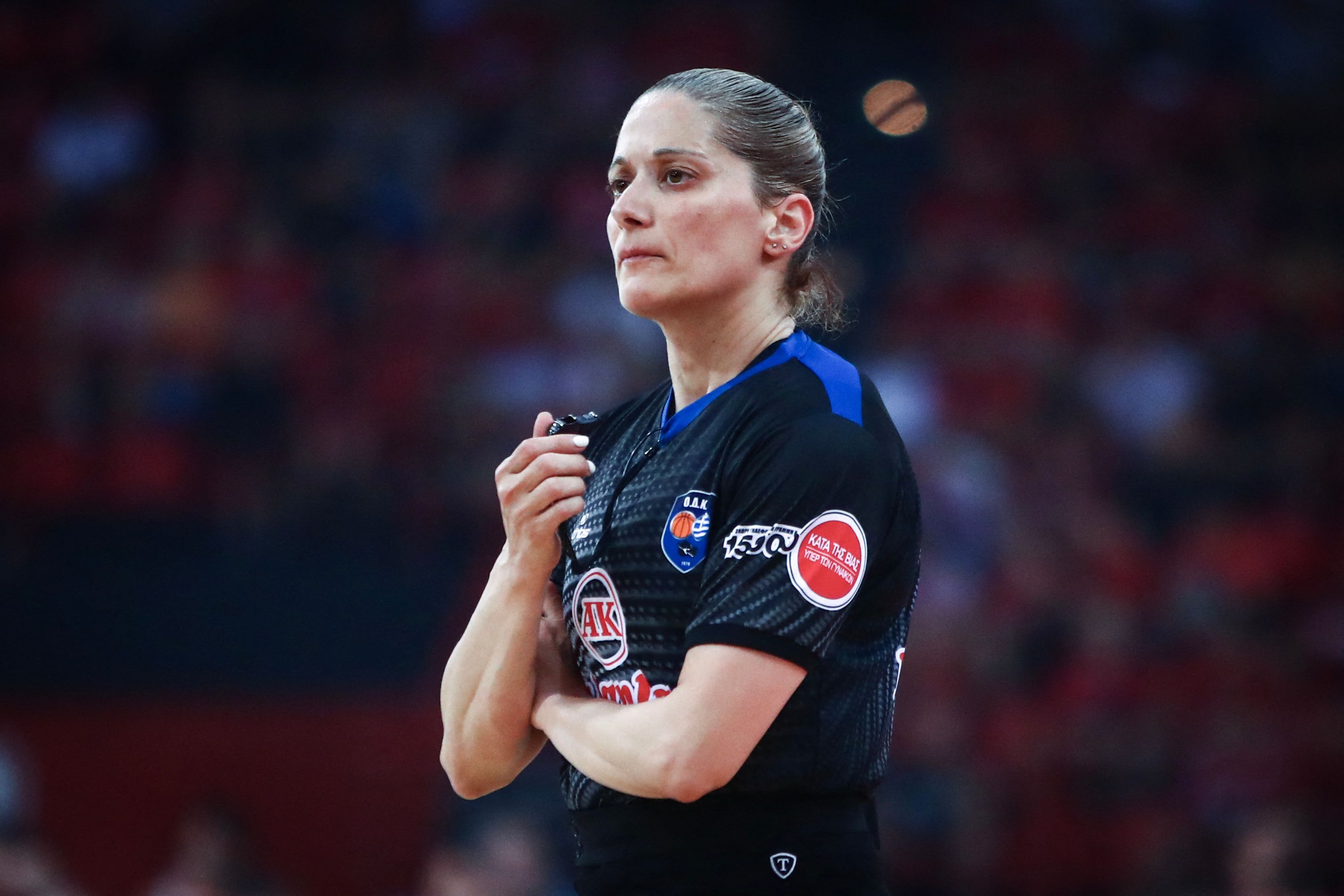Die Schiedsrichterin Vasiliki Tsaroucha steht in ihrem dunkelgrau-blauen Trikot auf dem Basketballfeld und blickt mit ernster Miene zur Seite.