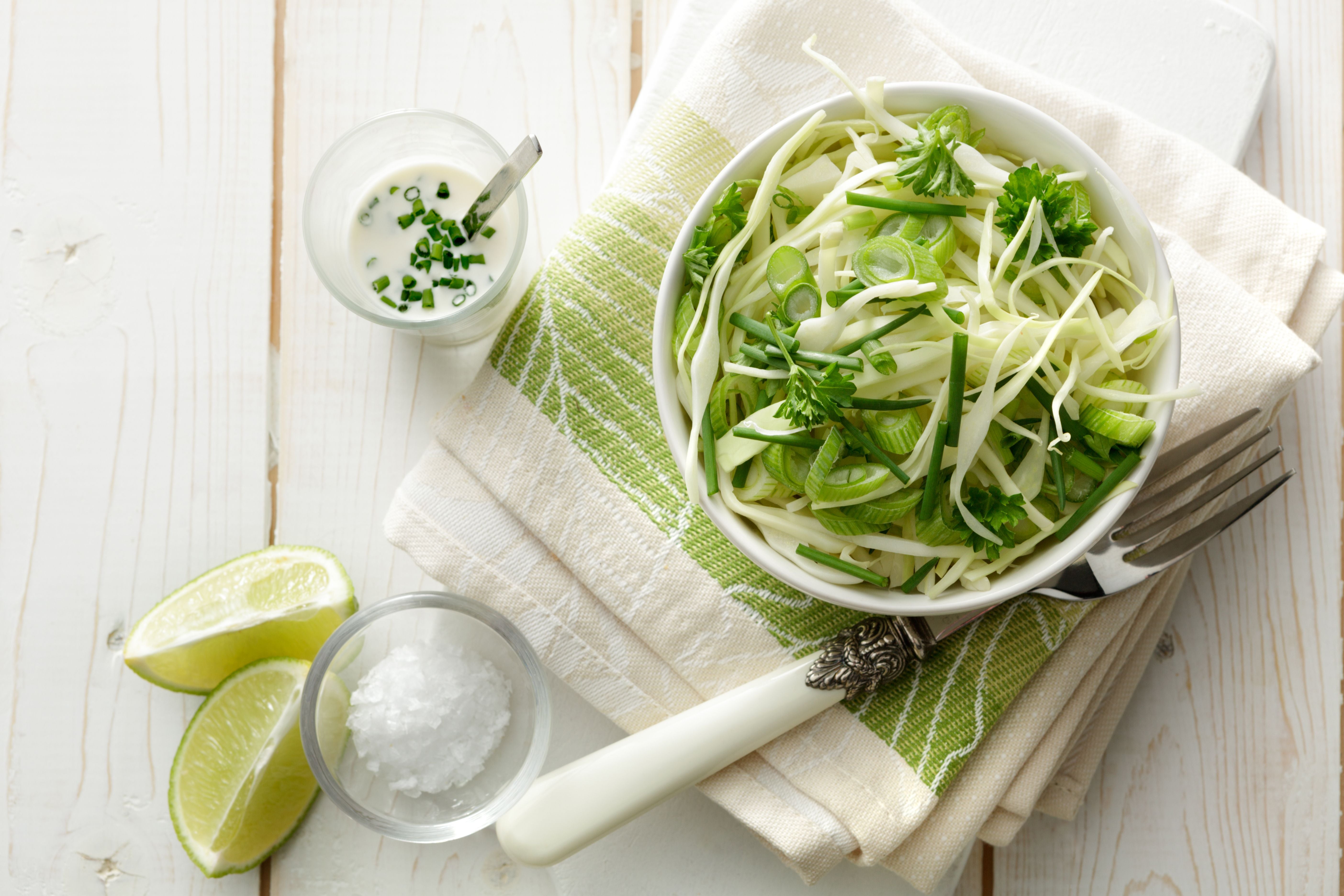 Schüssel mit Krautsalat, Limettenspalten, Salz und Dressing auf einem Geschirrtuch serviert.
