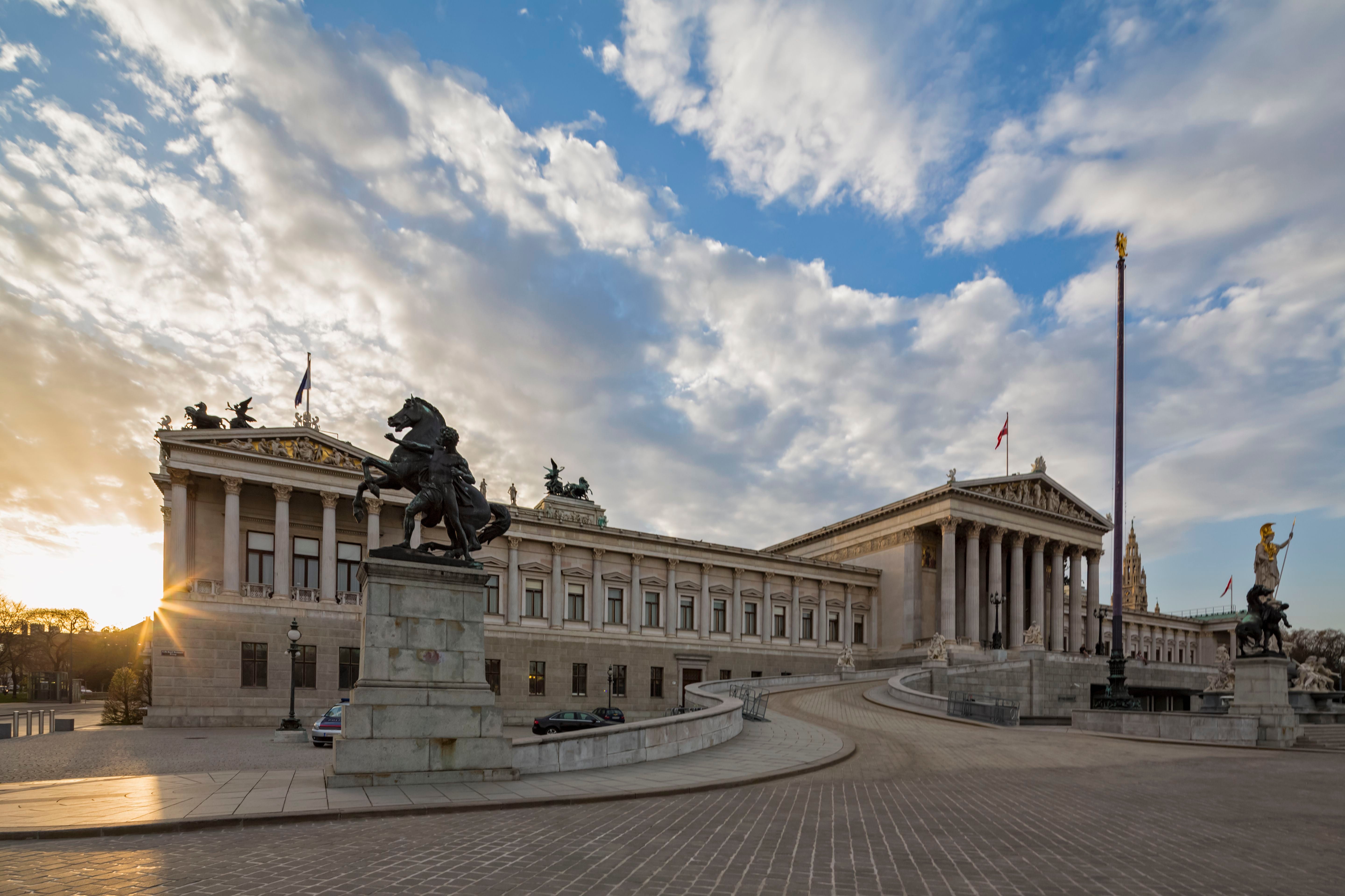 Das Parlamentsgebäude in Wien bei Sonnenuntergang mit Statuen im Vordergrund.