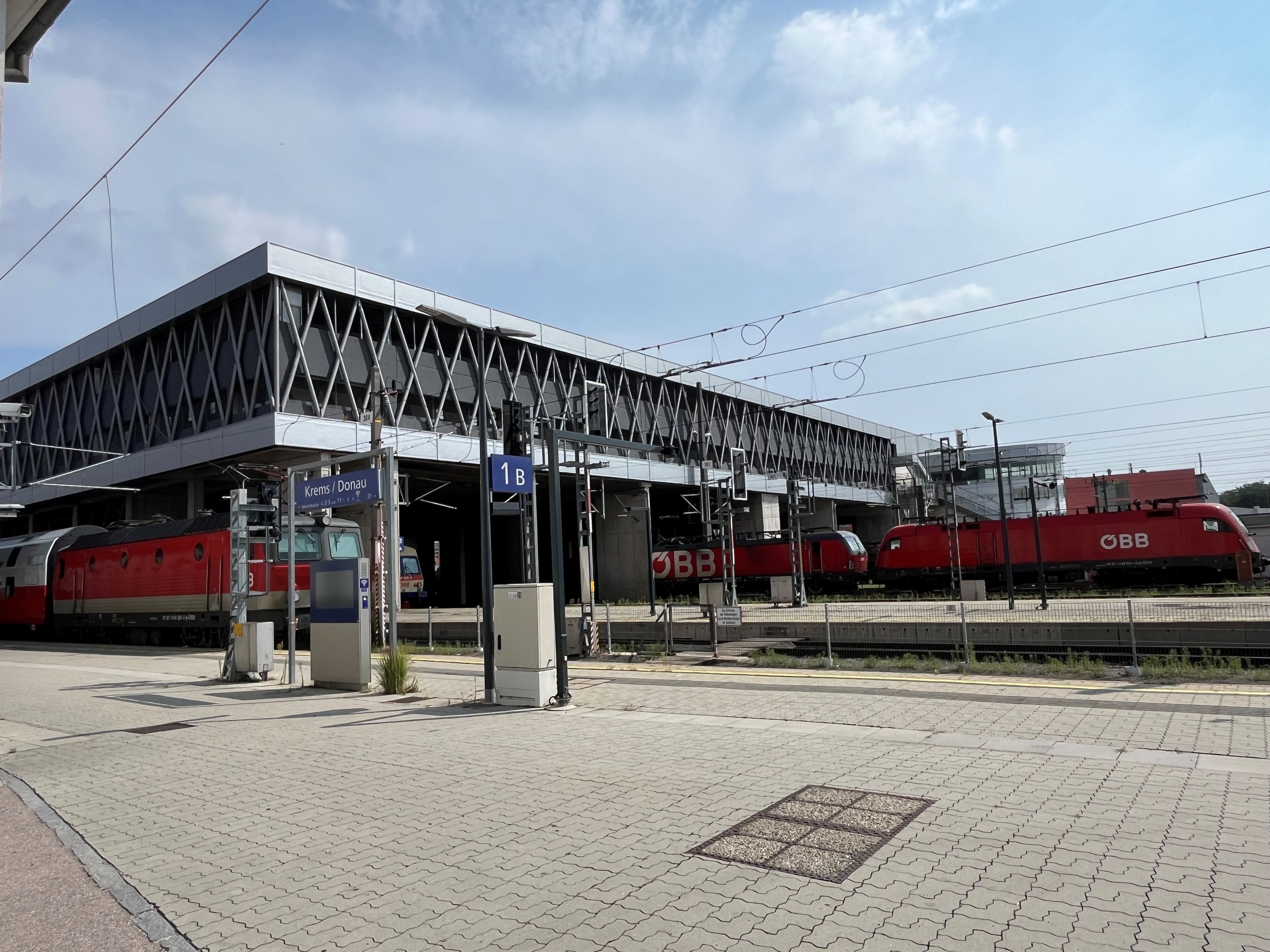 Modernen Bahnhof Krems mit roten ÖBB-Zügen auf den Gleisen bei Tageslicht.