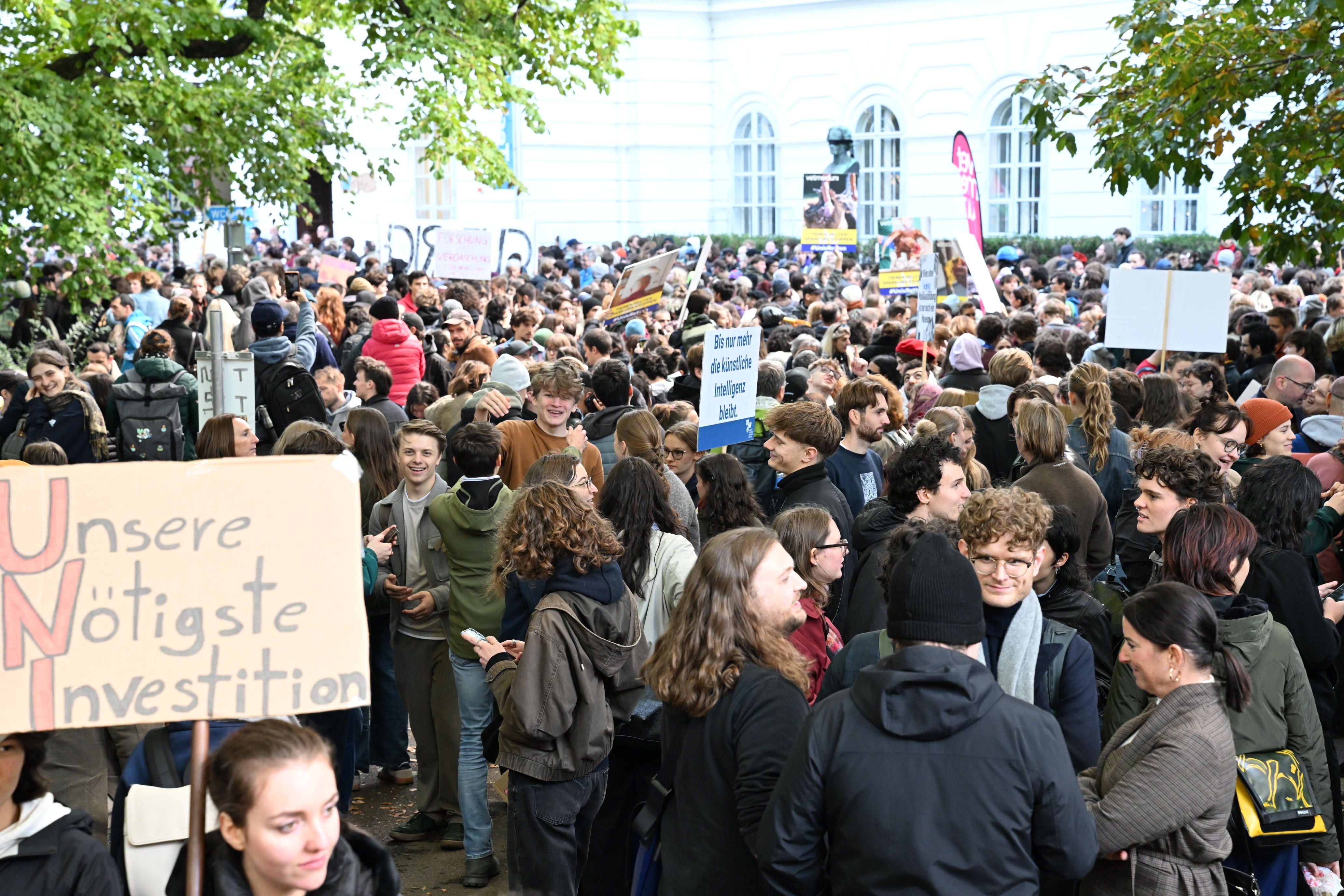 Viele Menschen nehmen an einer Demonstration mit Schildern vor einem weißen Gebäude teil.