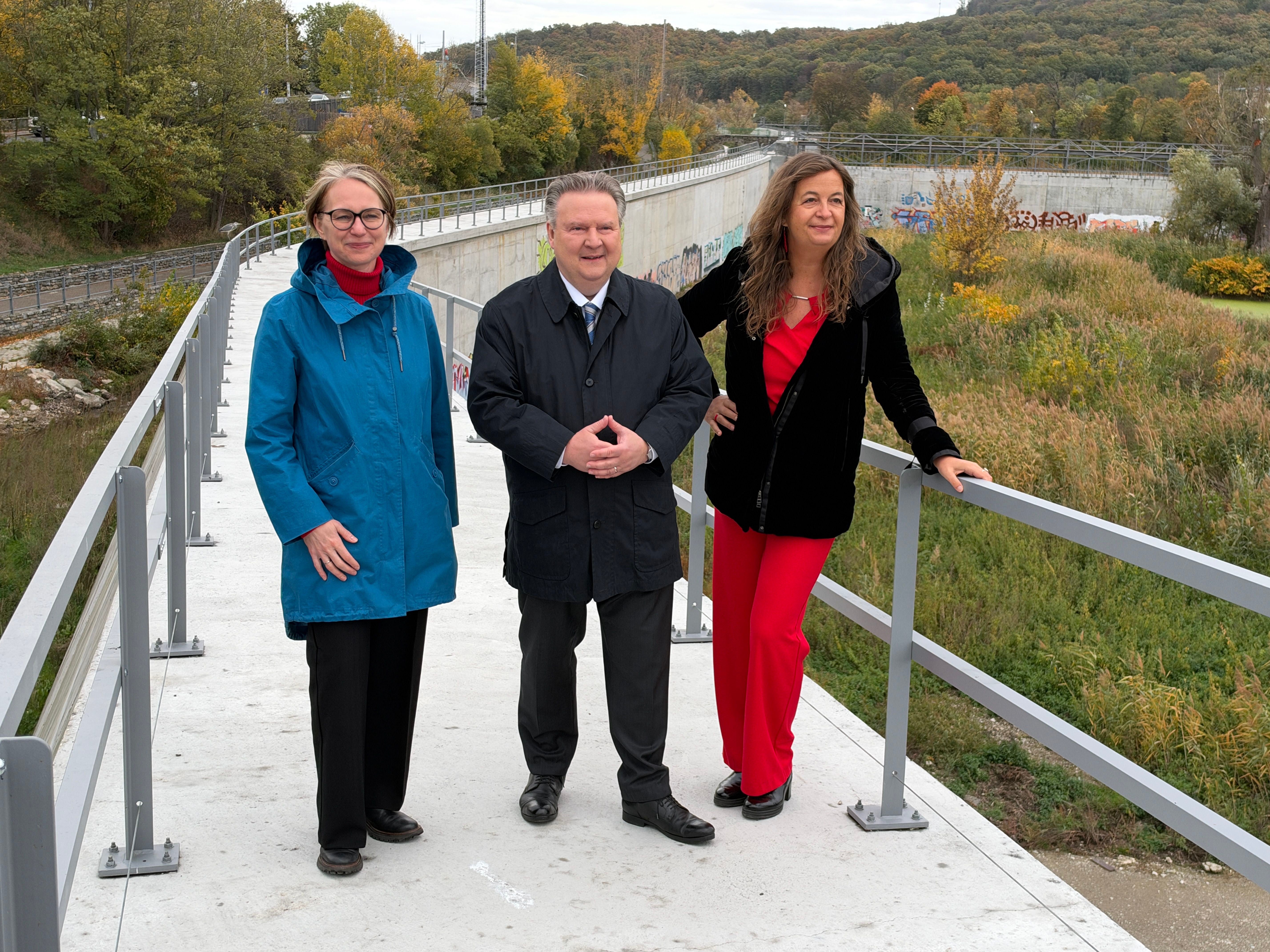 Drei Personen stehen auf einer neuen Hochwasserschutzanlage im Freien.