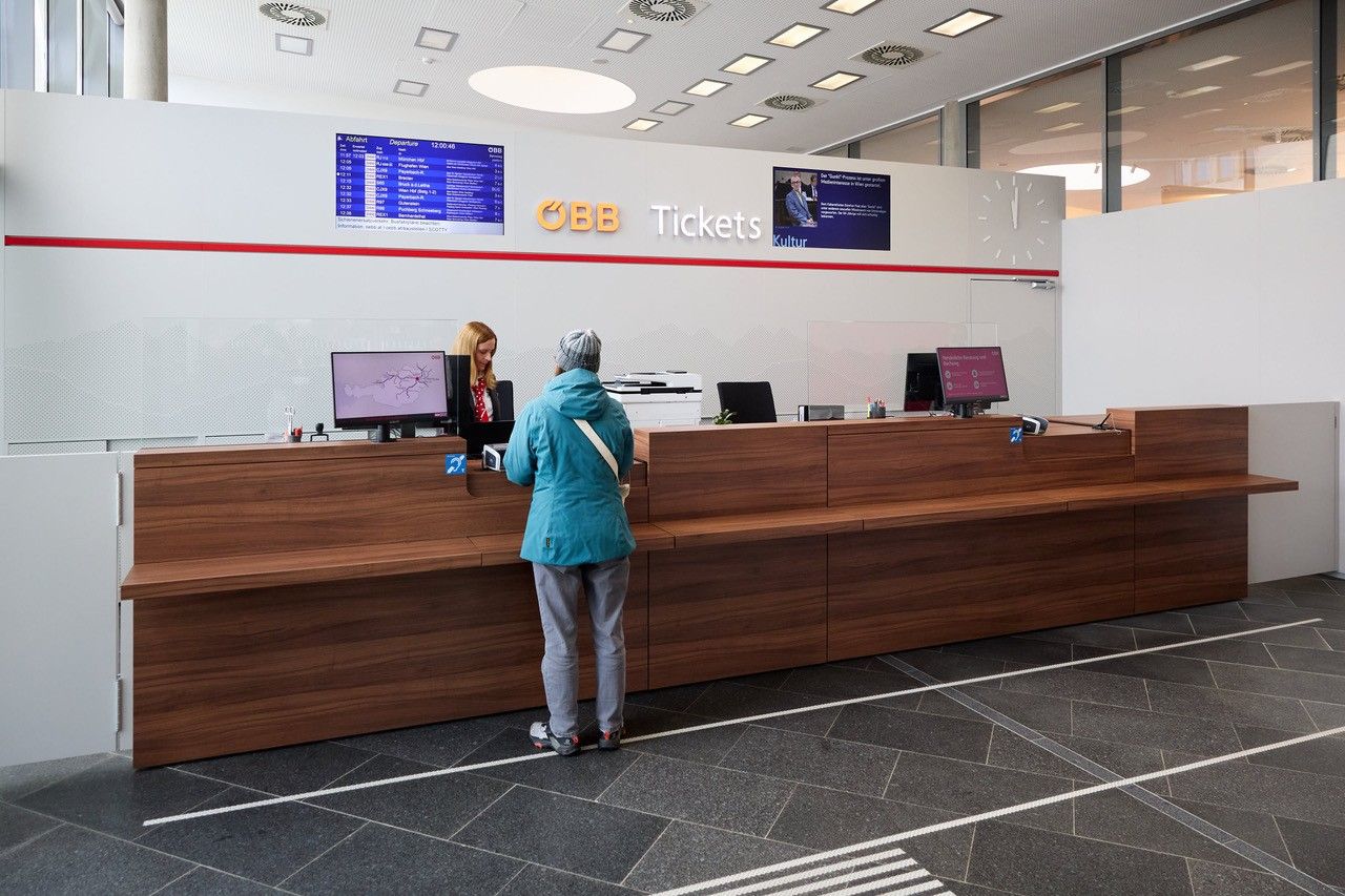 Person am Schalter im ÖBB-Reisezentrum Wiener Neustadt beim Kauf von Bahntickets.