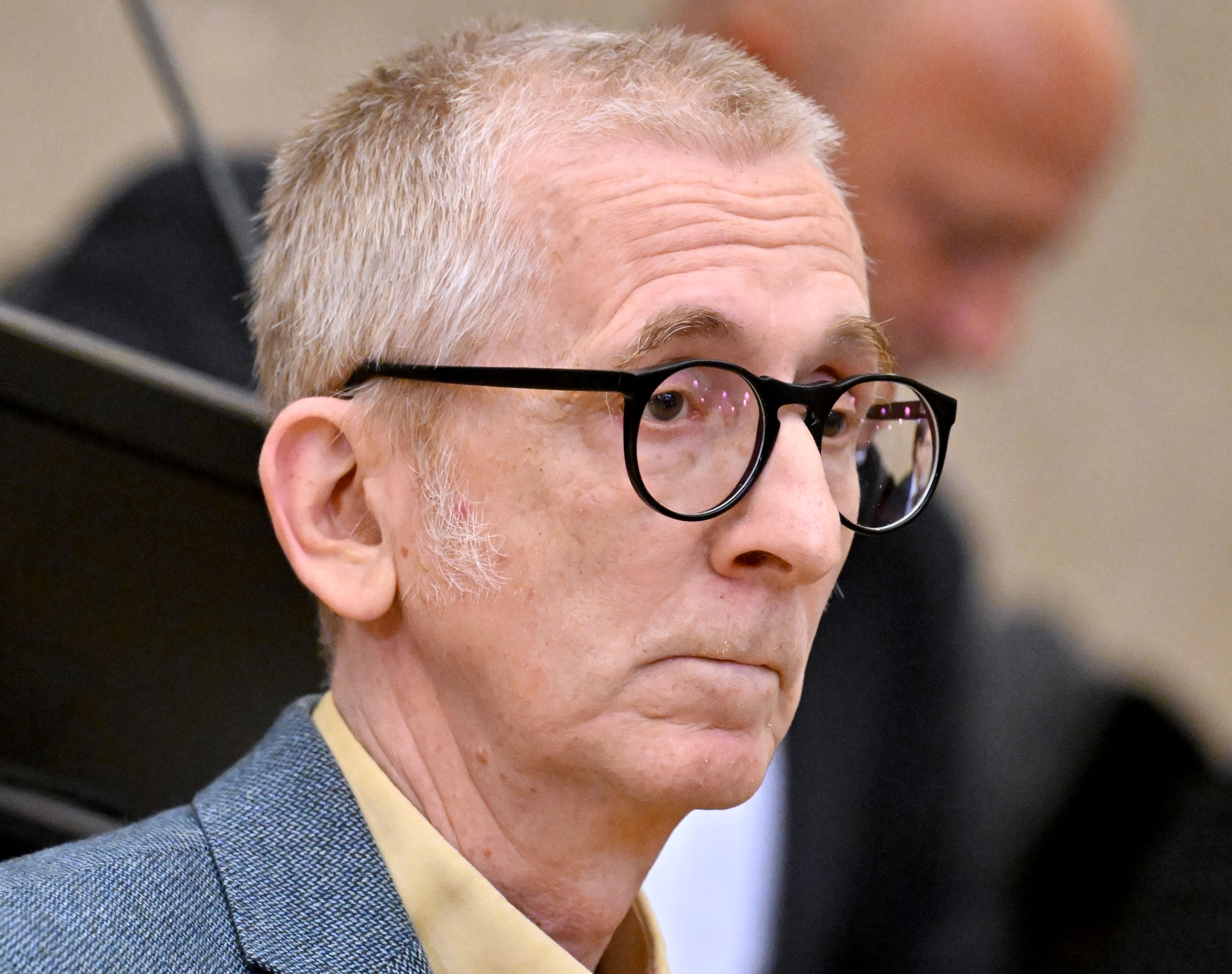Ein älterer Mann mit Brille und kurzem Haar sitzt in einem Gerichtssaal.