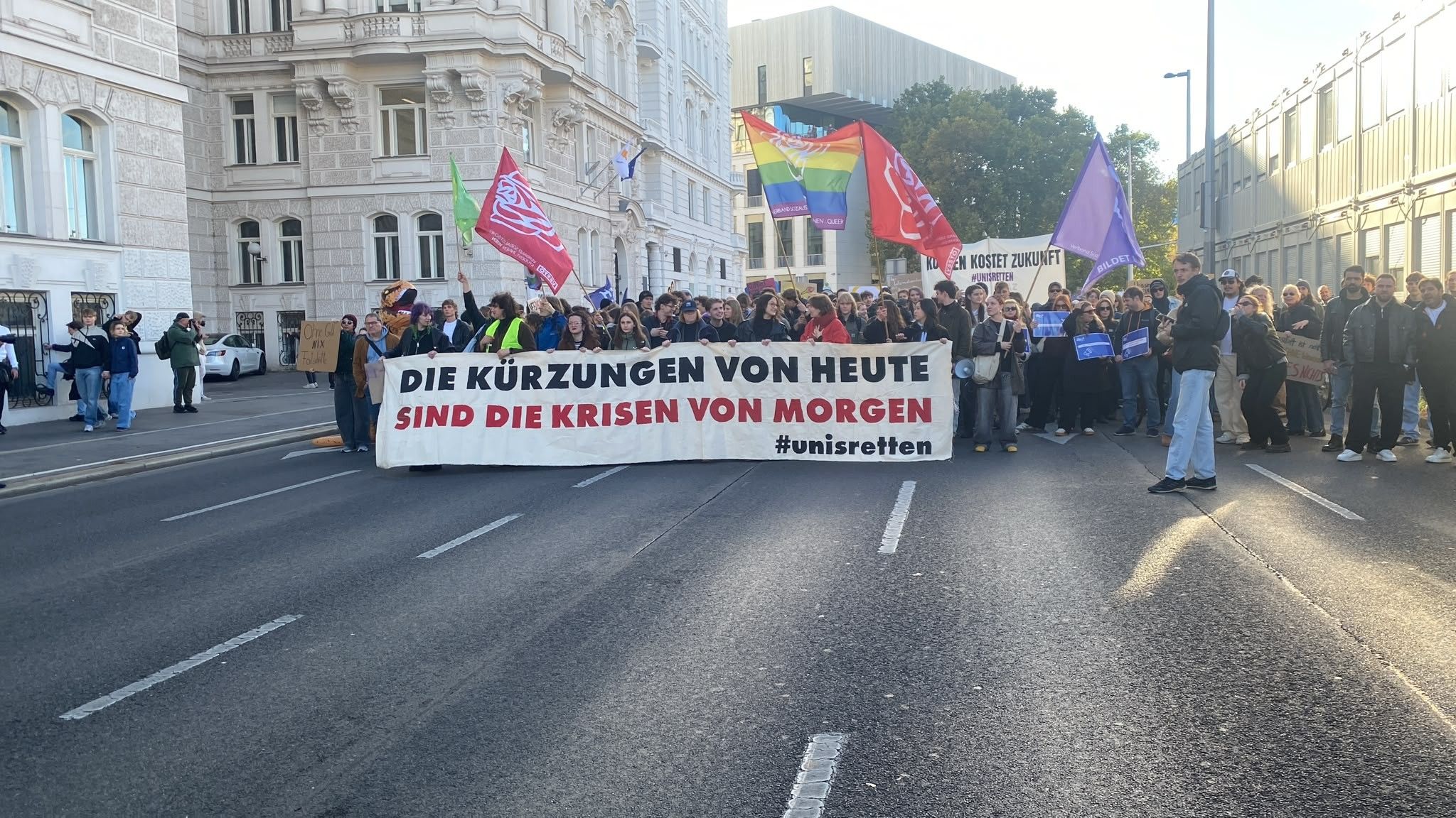 Demonstrierende Menschen halten Banner mit der Aufschrift „Die Kürzungen von heute sind die Krisen von morgen“.