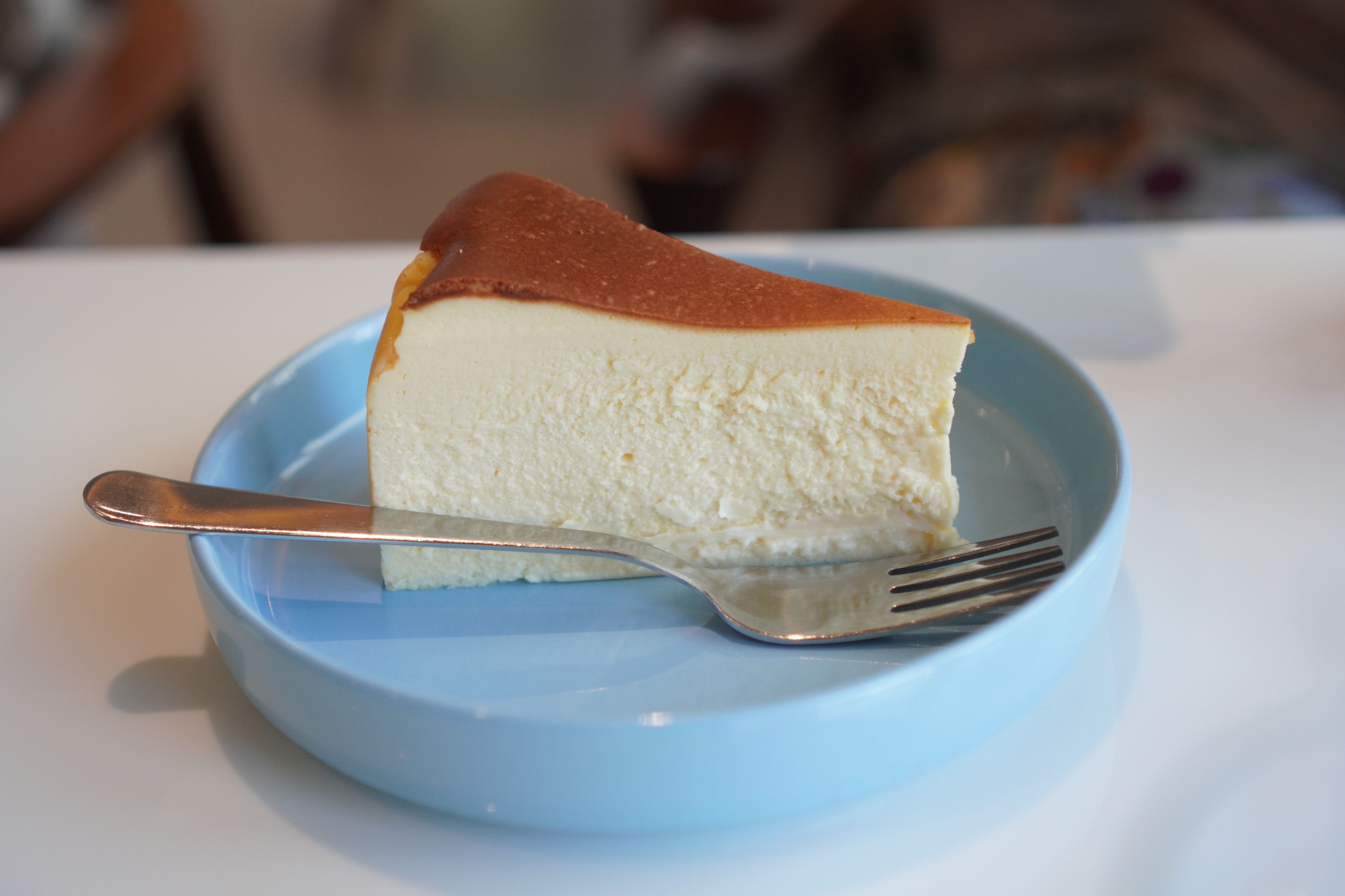 Ein Stück Käsekuchen auf einem blauen Teller mit einer Gabel.