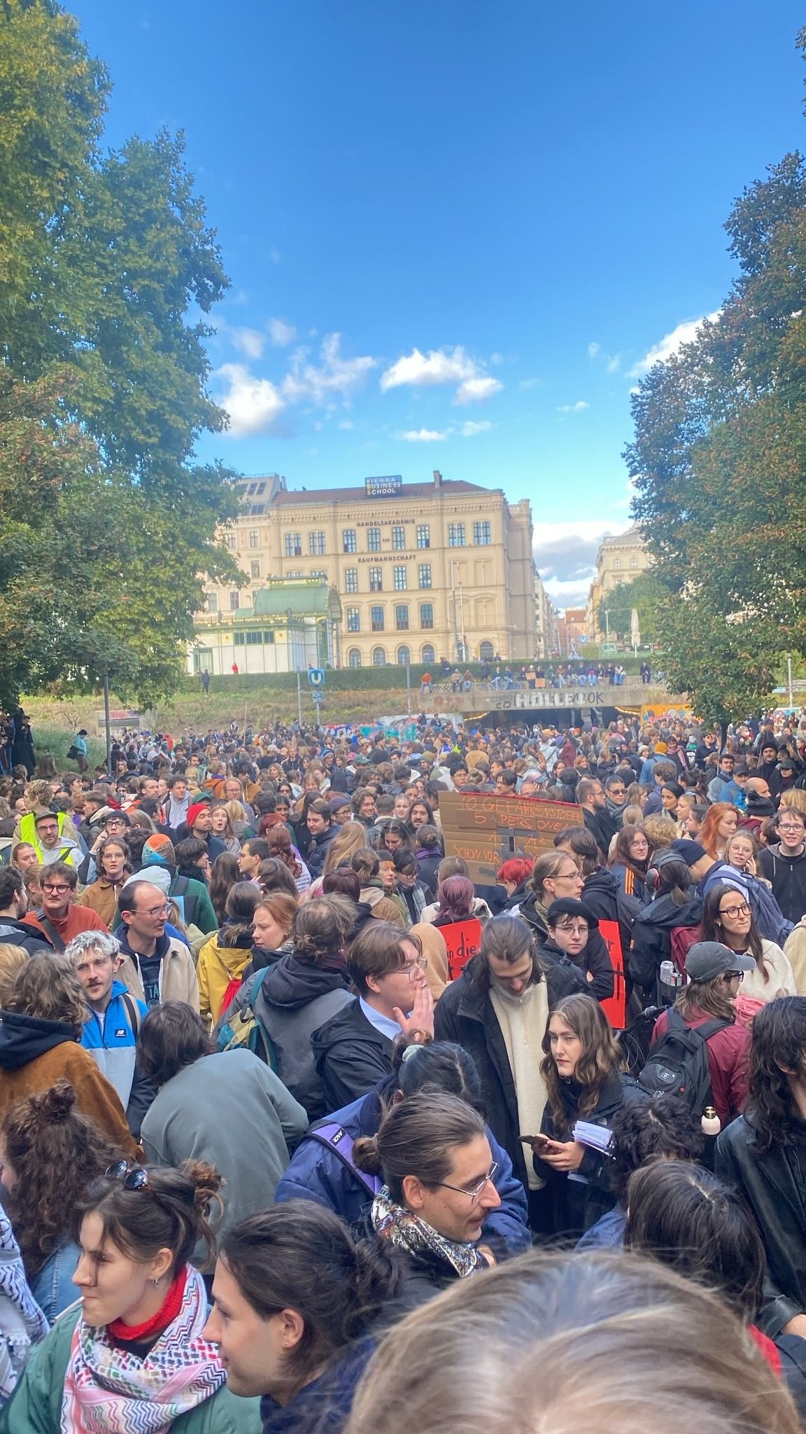 Große Menschenmenge bei einer Demo im Freien vor historischen Gebäuden unter blauem Himmel.