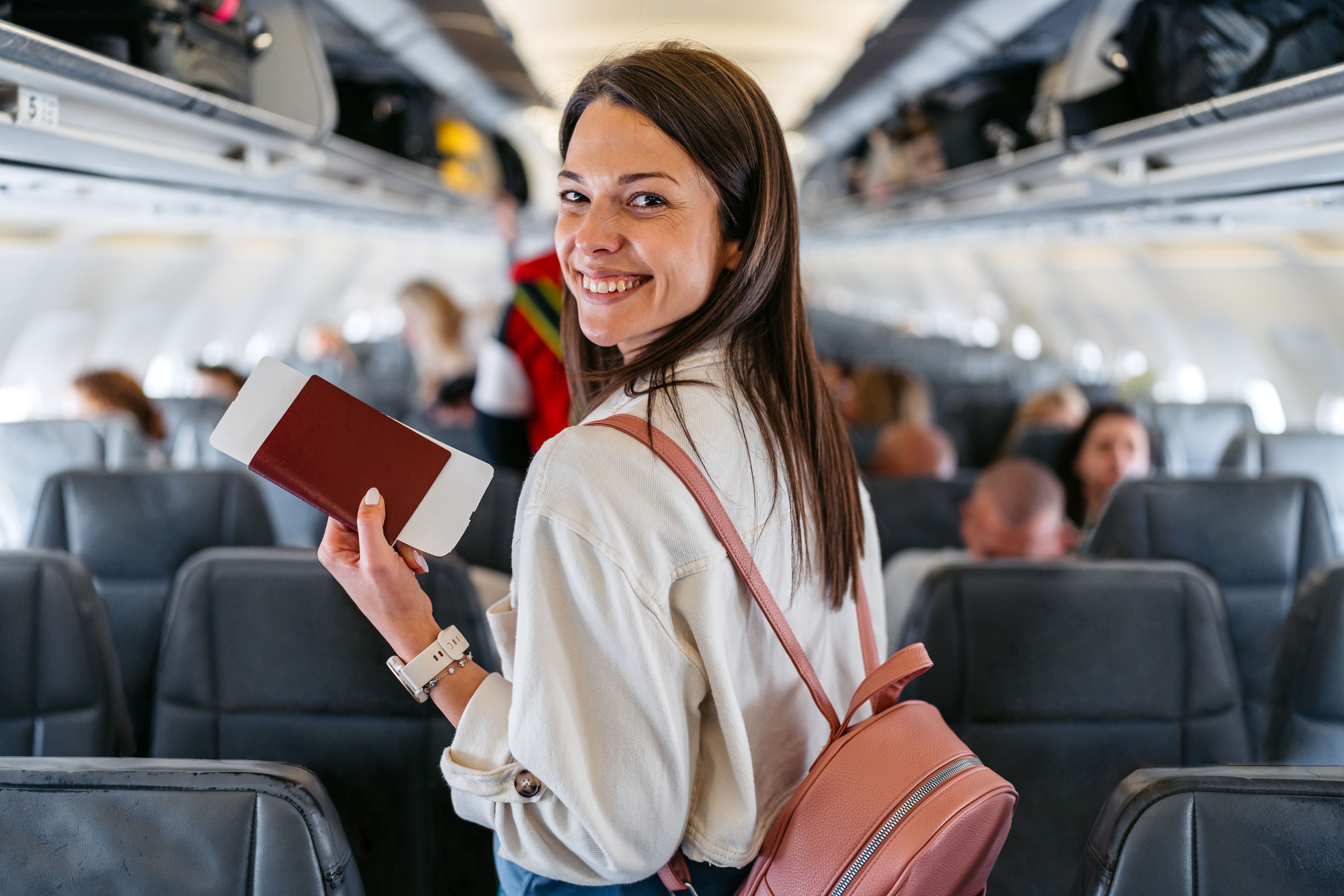 Junge Frau mit Rucksack und Ticket lächelt beim Einsteigen ins Flugzeug und sucht ihren Sitzplatz.