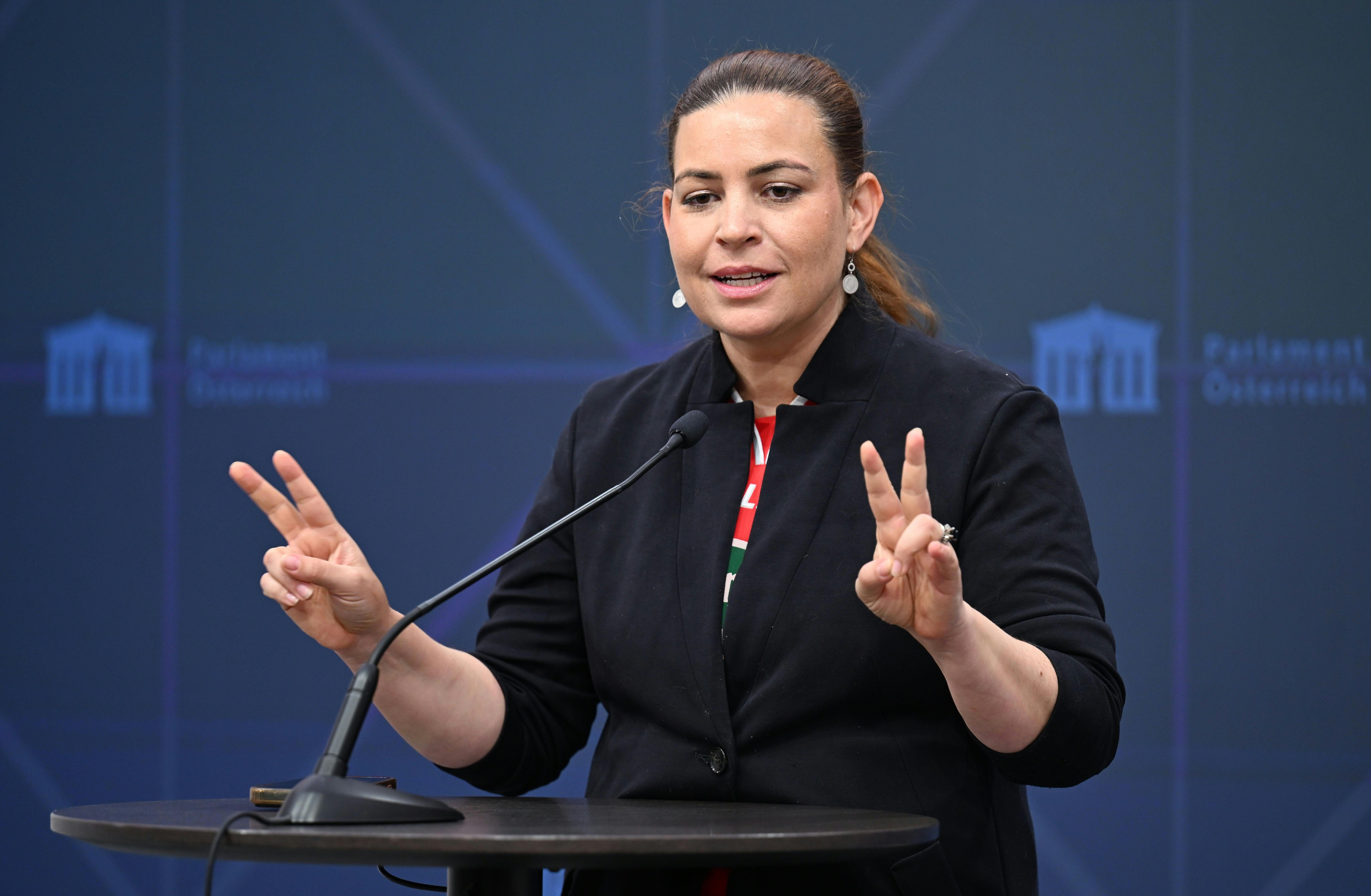 Eine Frau spricht im Parlament am Rednerpult und hält an beiden Händen ein Victory-Zeichen.