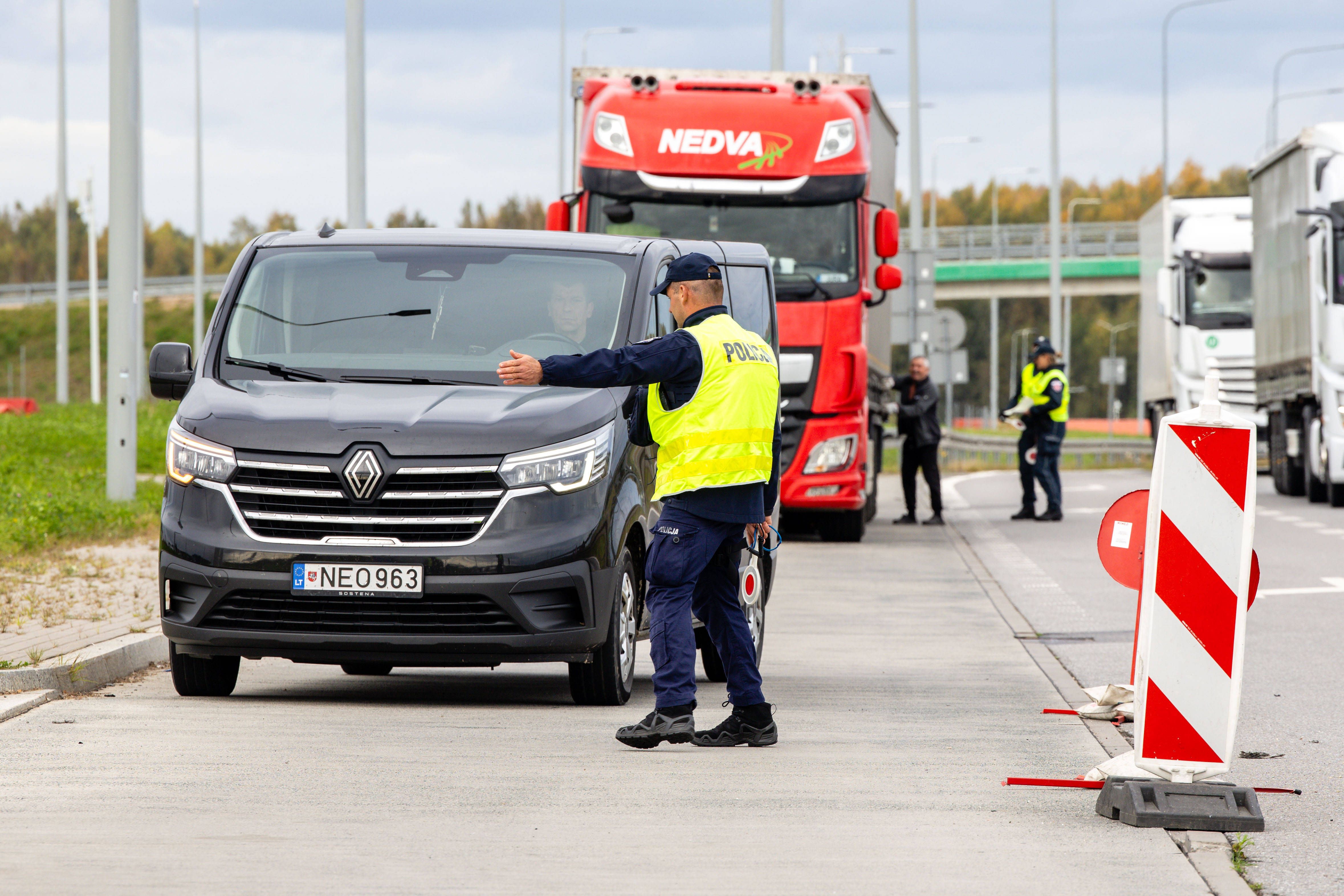 Polizist kontrolliert Fahrer an einem Grenzkontrollpunkt, Lkw warten im Hintergrund.