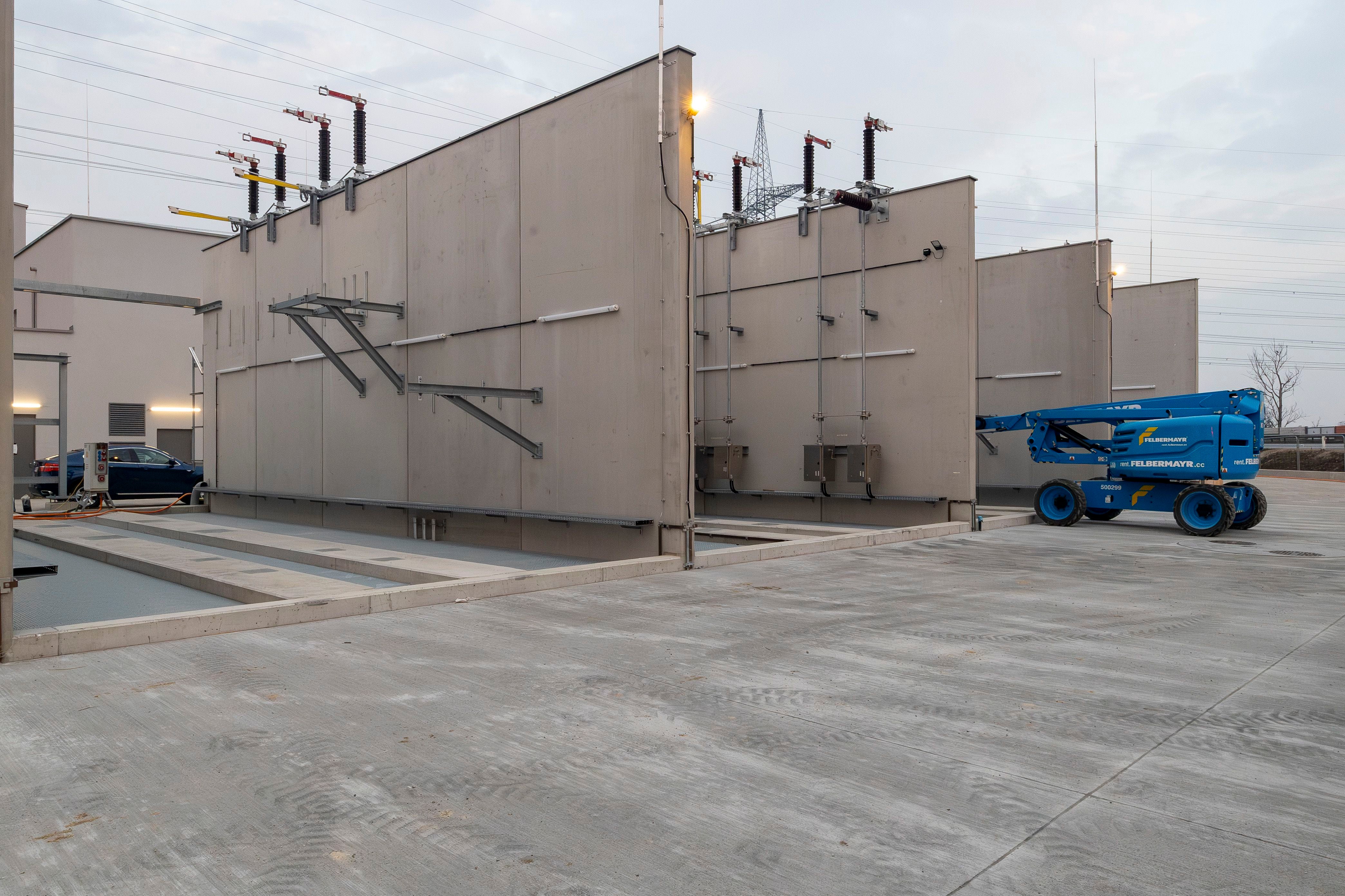 Großer Trafo im Umspannwerk Achau mit Betoneinfassungen und einer blauen Hebebühne.