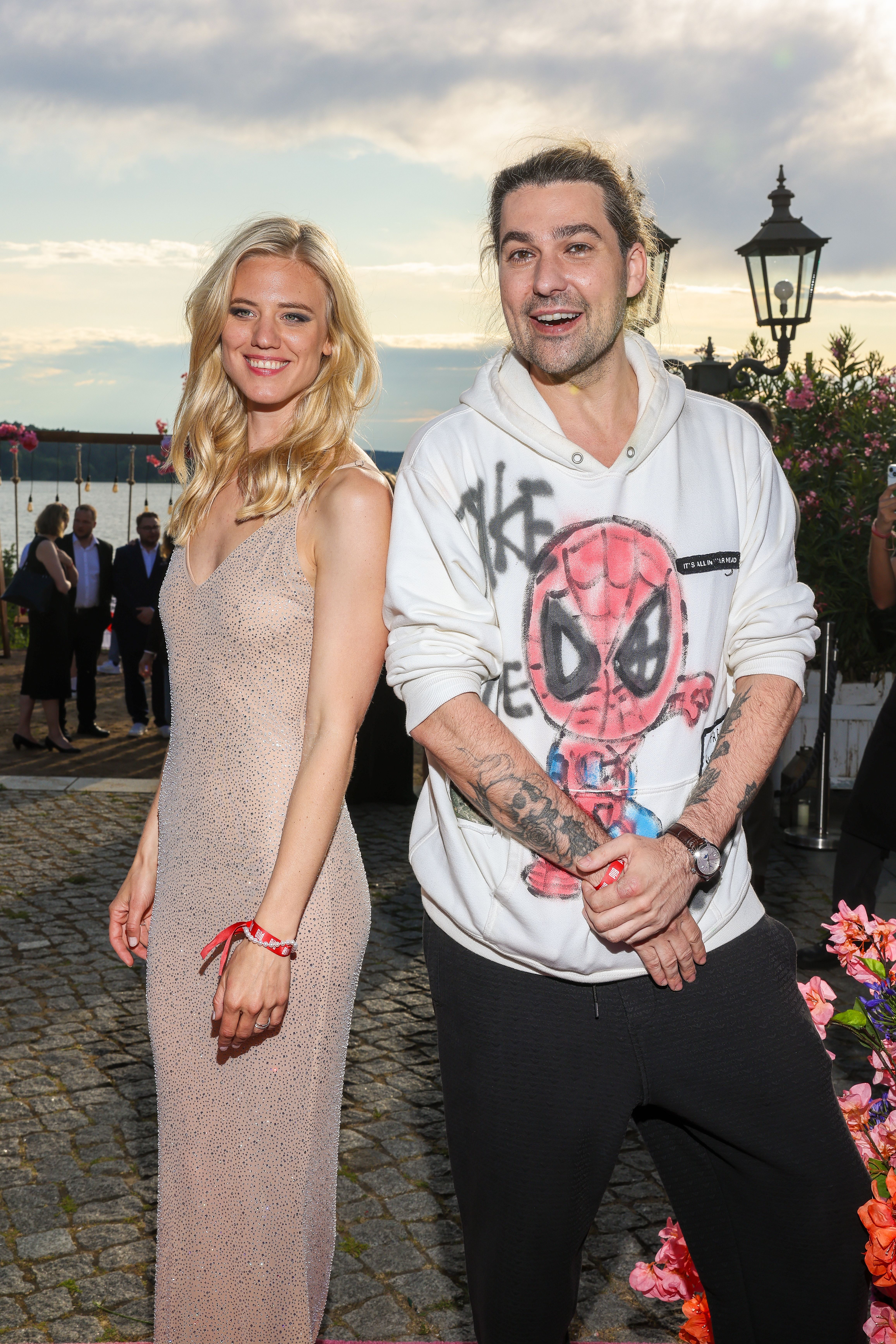 Eine Frau im Abendkleid und ein Mann im Hoodie mit Spiderman-Print posieren lachend im Freien.
