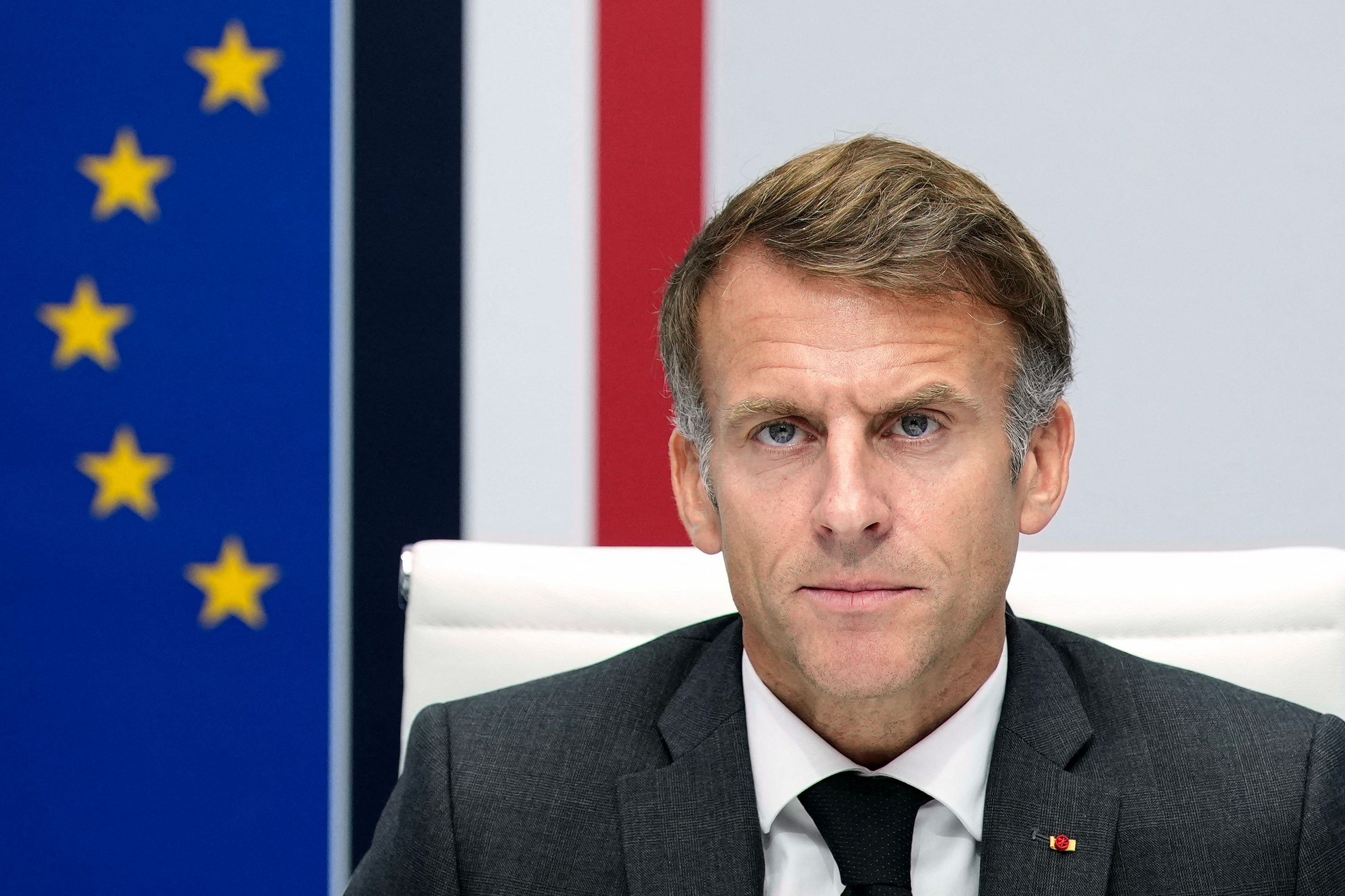 Emmanuel Macron sitzt in Anzug und Krawatte vor EU- und Frankreich-Flaggen.