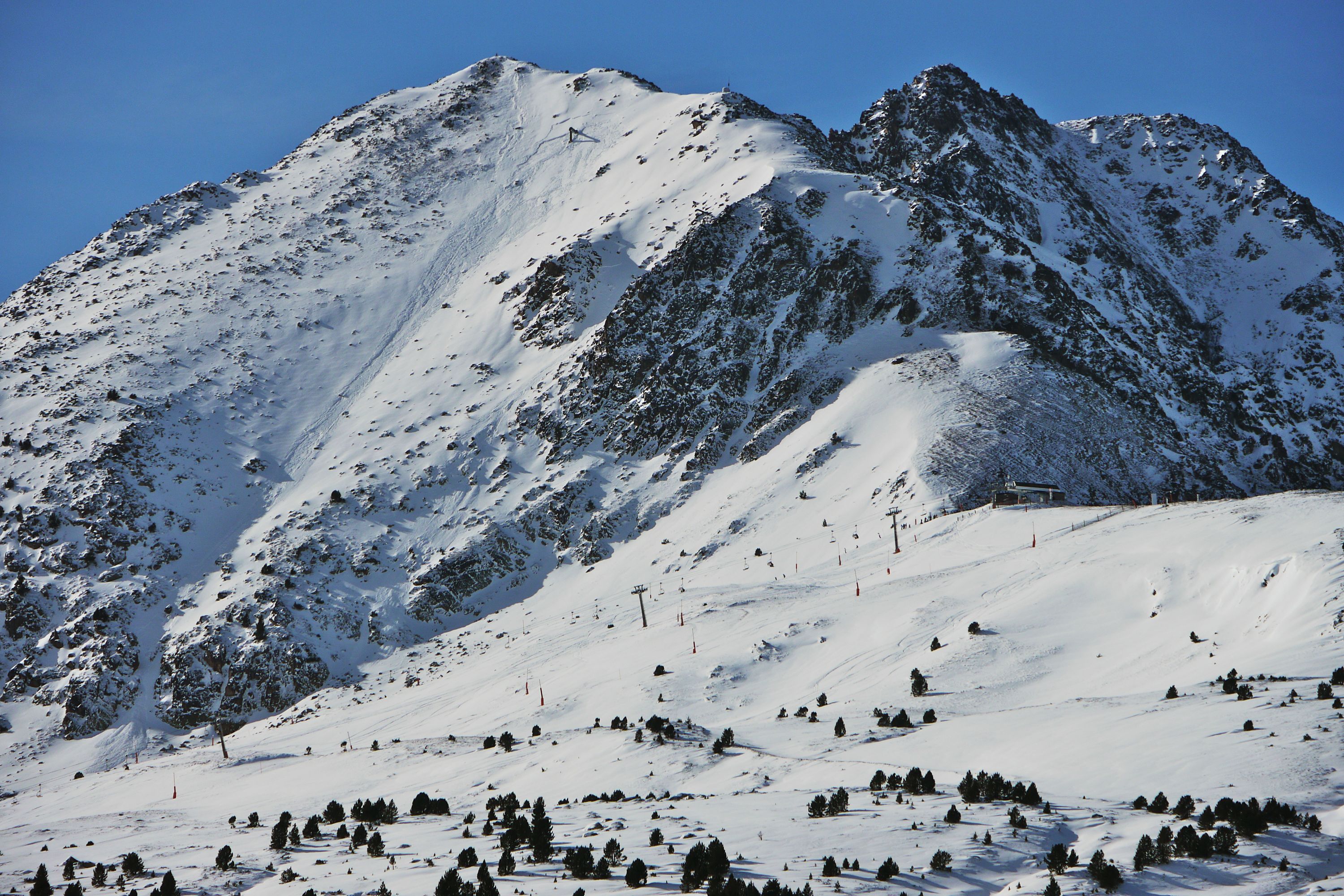 Verschneite Berge in Andorra mit Skipisten und vereinzelten Bäumen im Vordergrund.