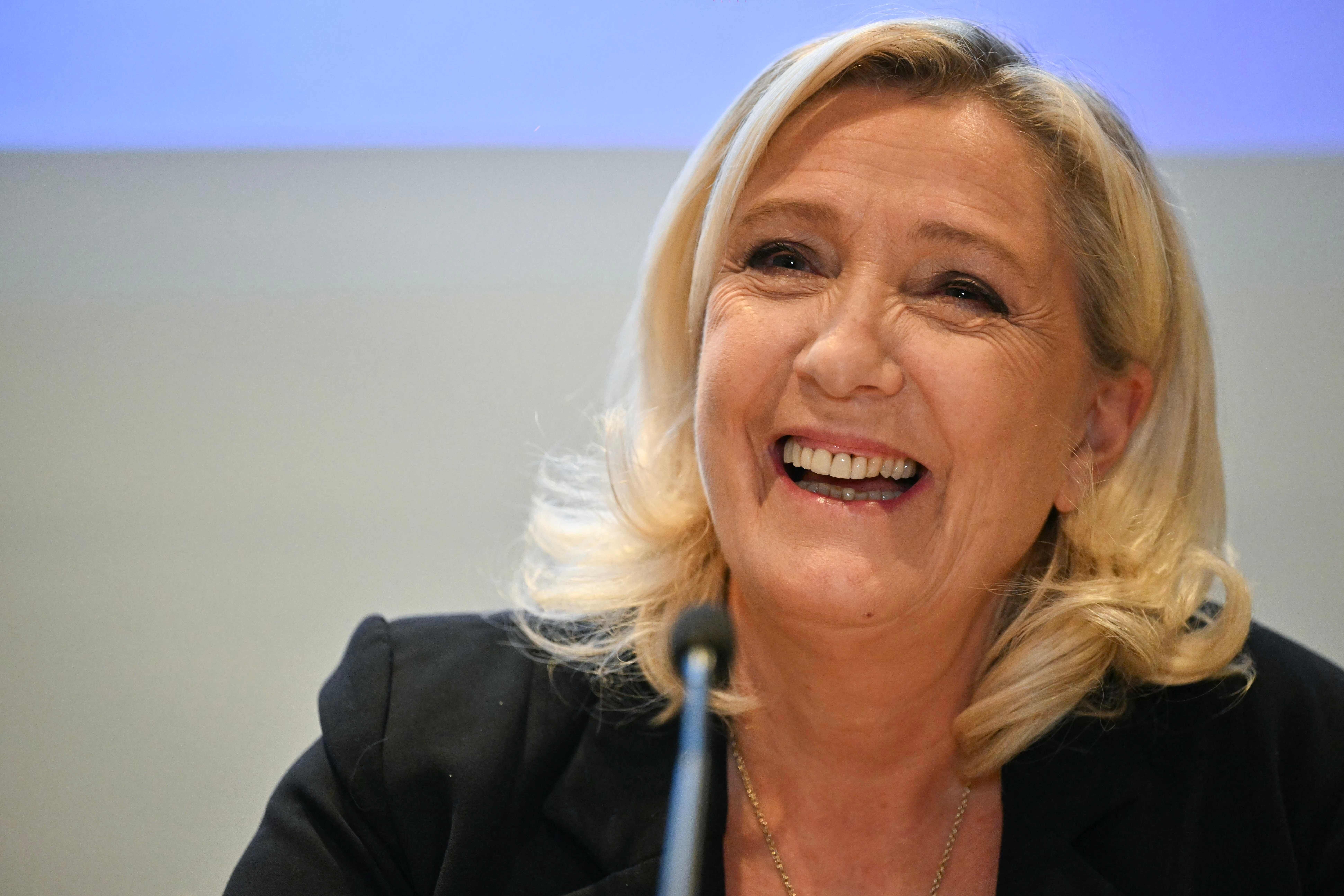 Eine blonde Frau lächelt bei einer Pressekonferenz, im Vordergrund ist ein Mikrofon sichtbar.